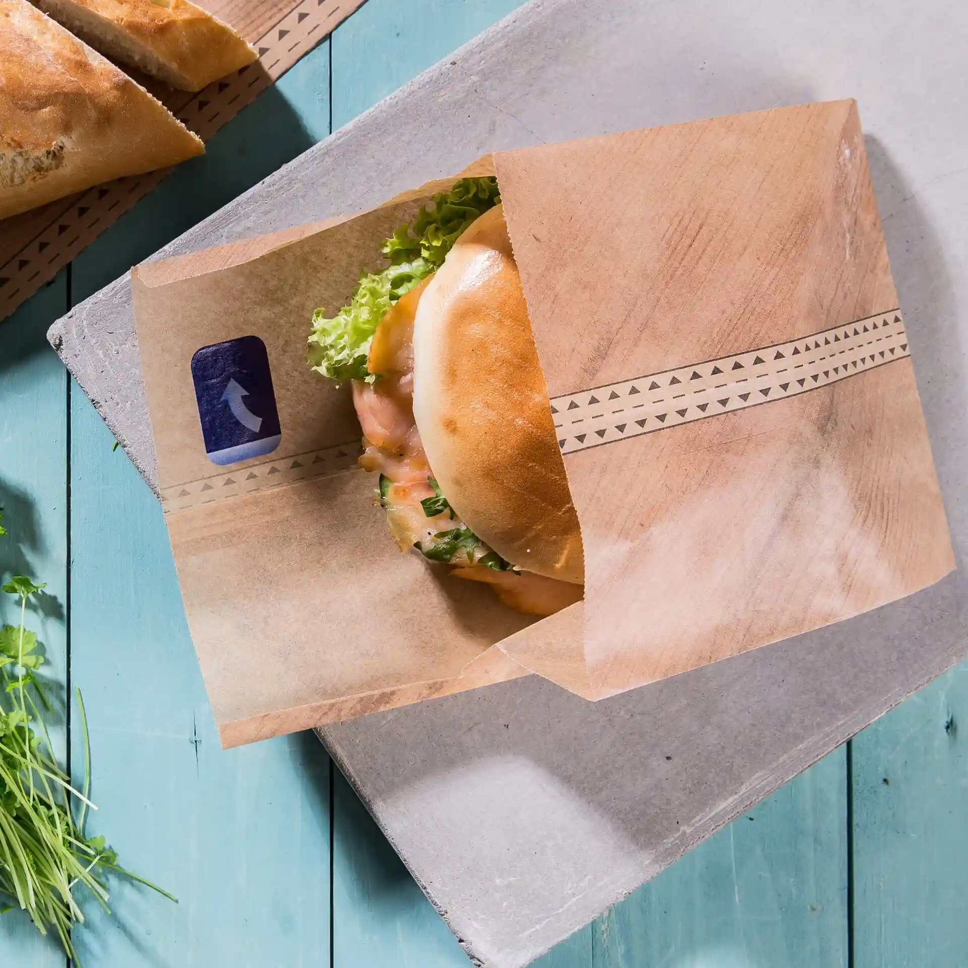 Brown paper bag containing a burger with lettuce, placed on a blue wooden surface.
