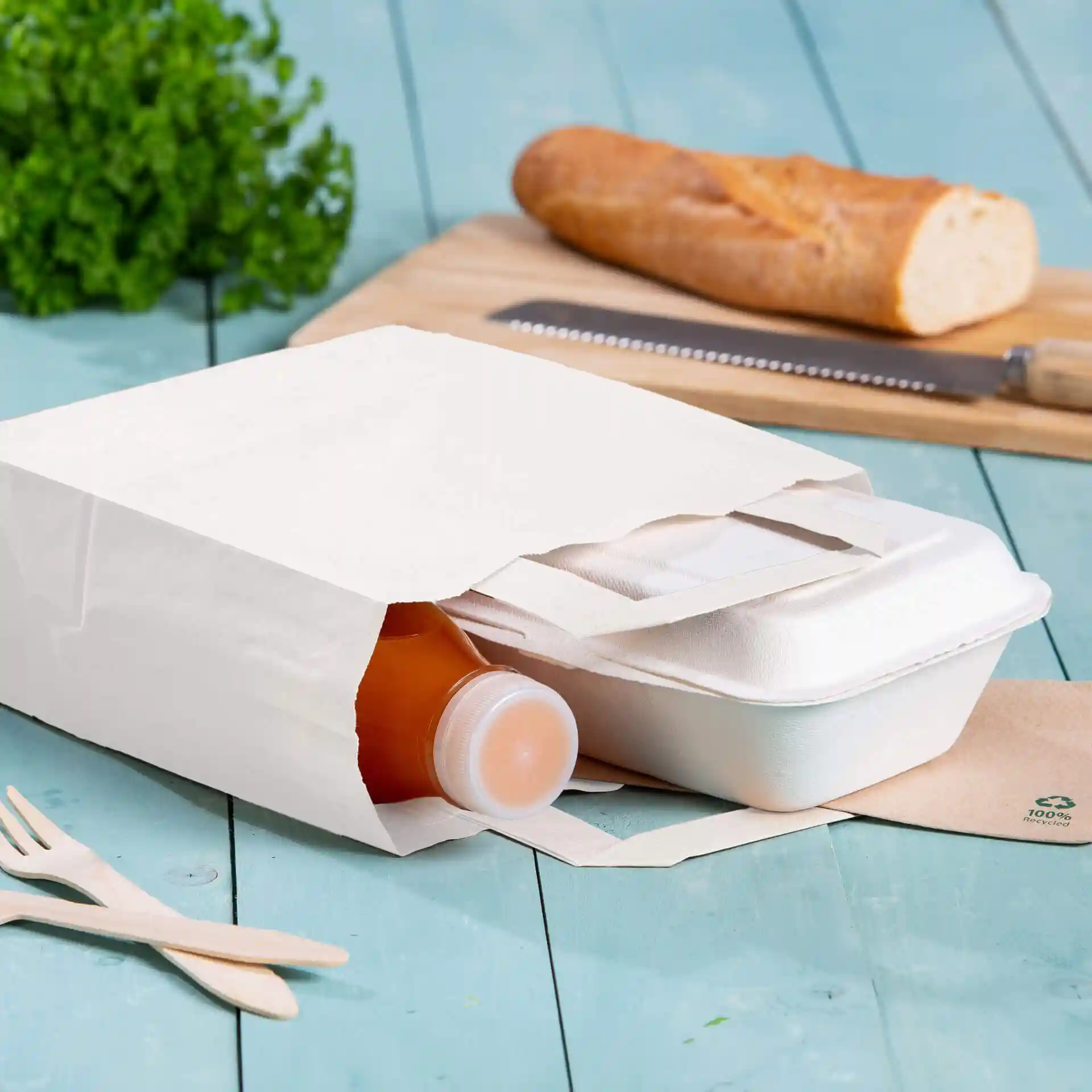 White kraft paper carrier bag with a bottle and a takeout container inside, placed on a blue wooden surface.