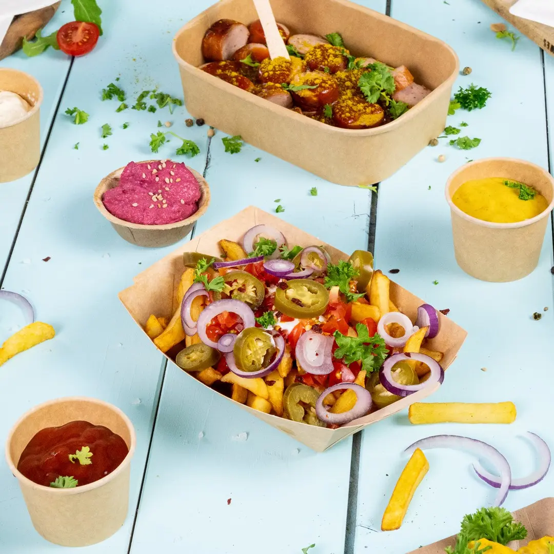 Image of various food items including a container of sausages, a box of loaded fries with toppings, and small cups of sauces on a blue wooden surface.