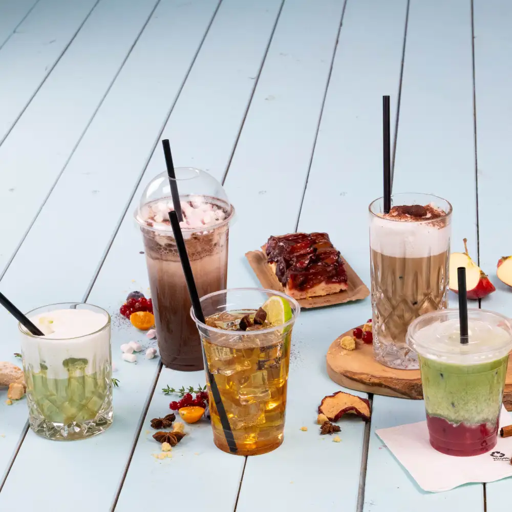 Various beverages displayed on a light blue wooden surface; drinks include a green smoothie, an iced tea, a coffee, and a dessert.