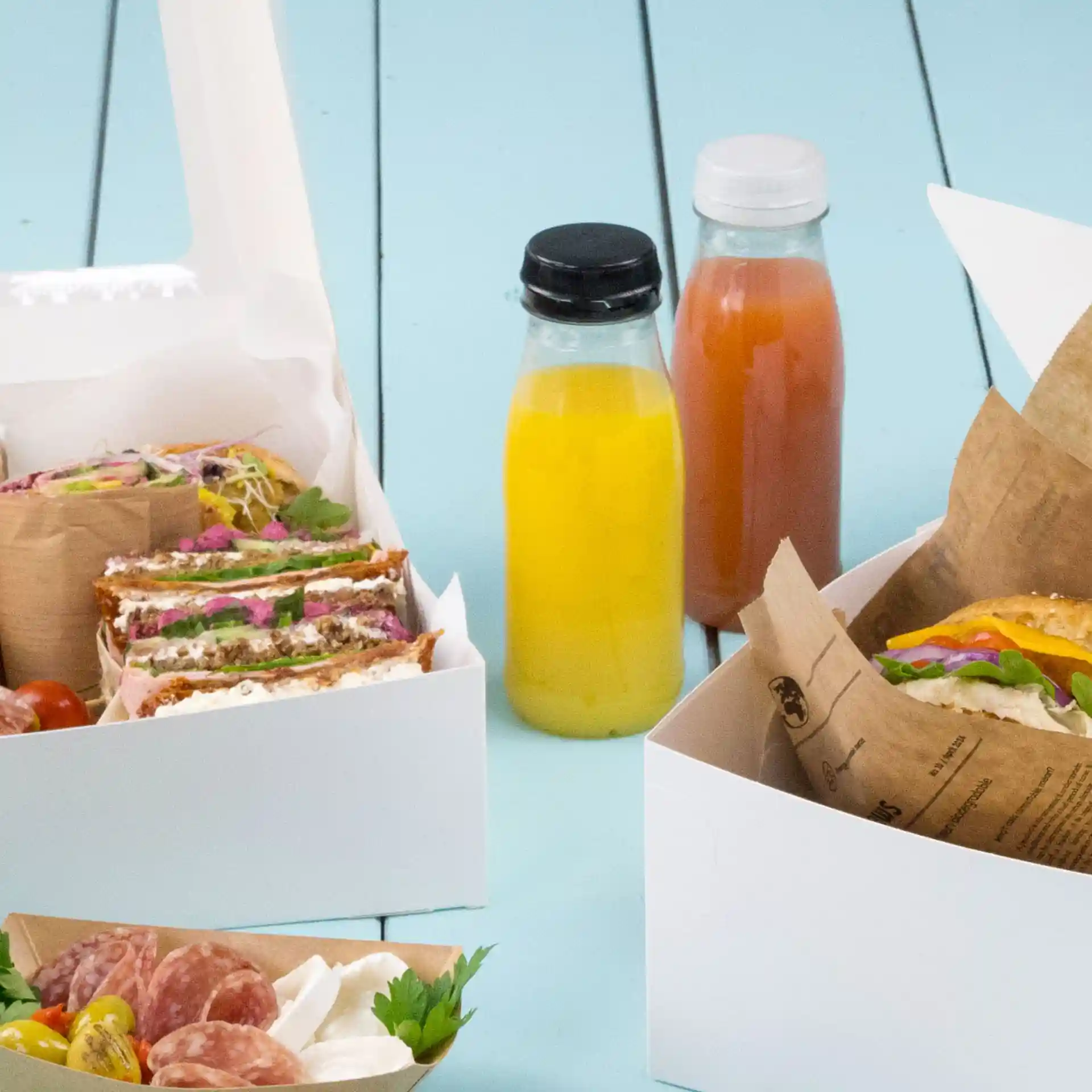 Image of food containers with sandwiches, a salad, and two clear bottles with black and white lids on a blue surface.