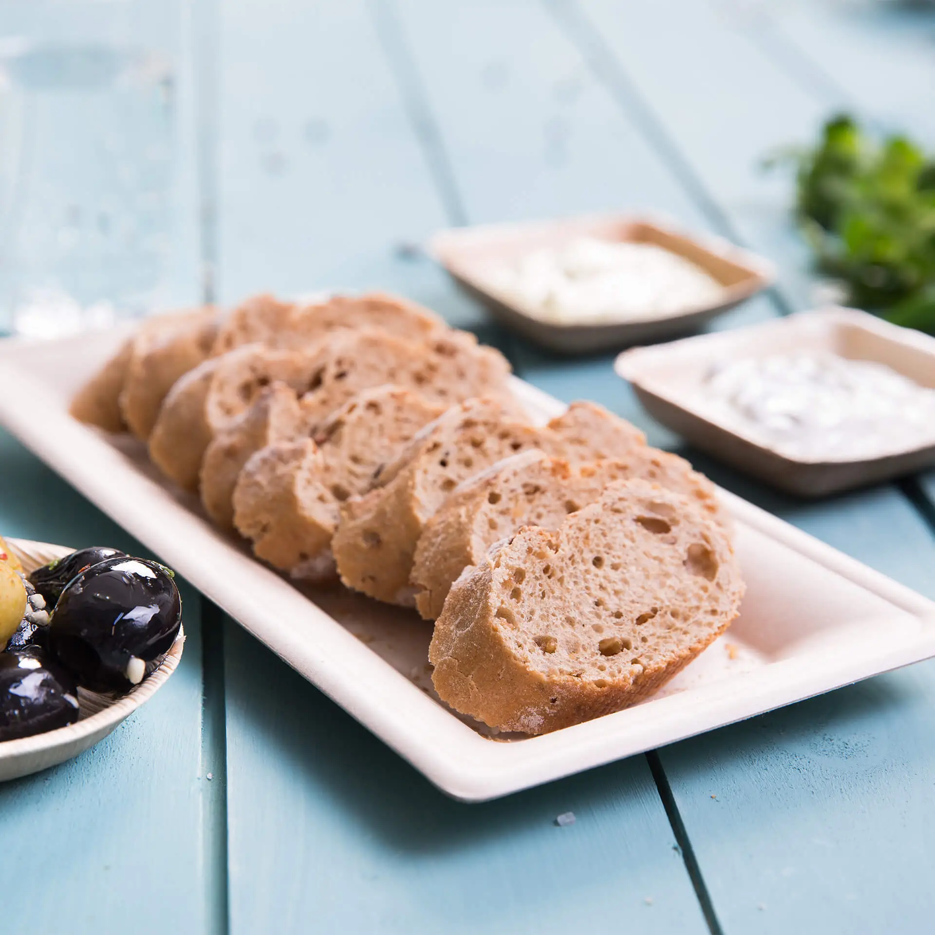 Sliced bread served on a rectangular sugarcane plate, with dips in small bowls nearby.