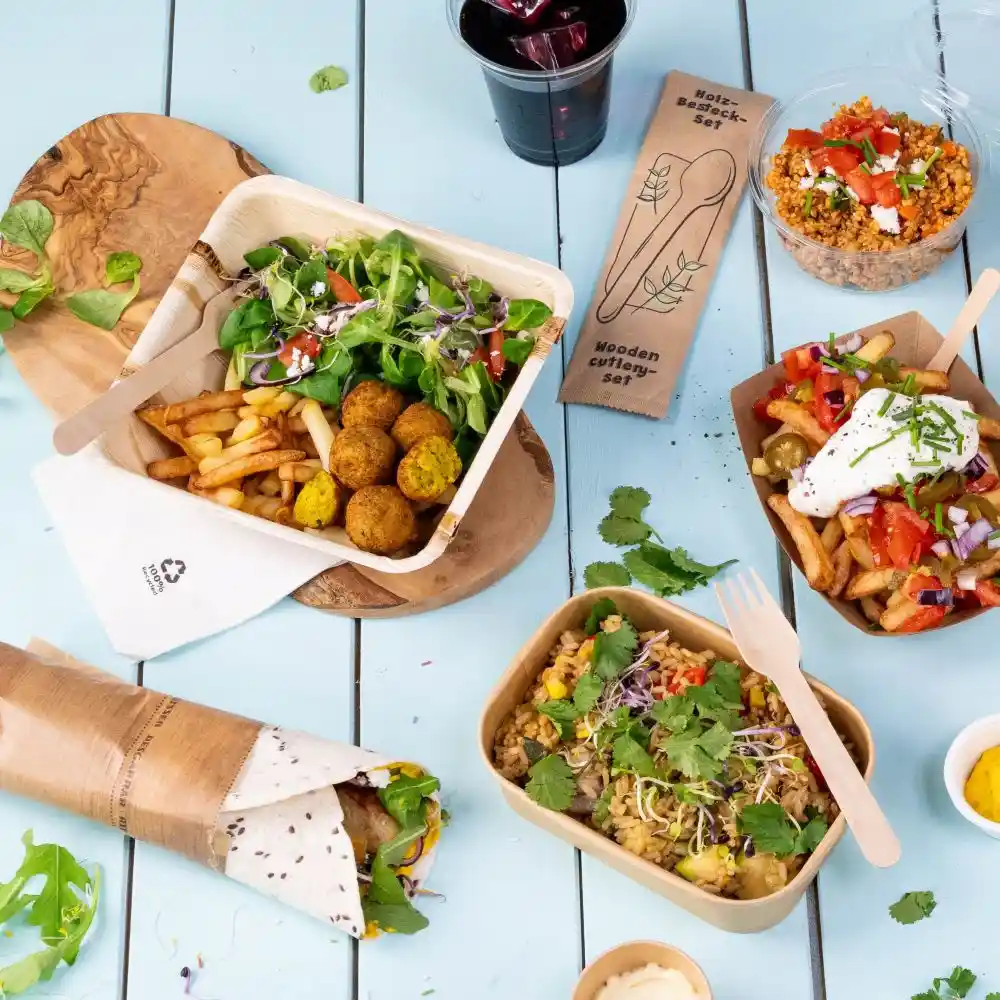 Assorted meal display with falafel, fries, salad, and rice bowl; accompanied by a cold drink and wooden cutlery set.
