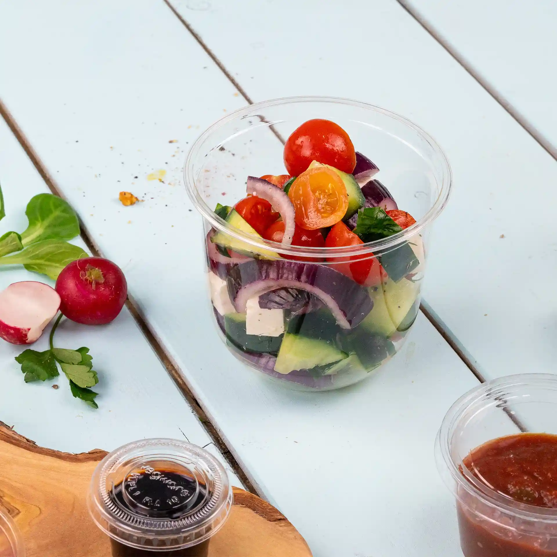Transparent cup filled with mixed salad ingredients, including cherry tomatoes, cucumber, and red onion.