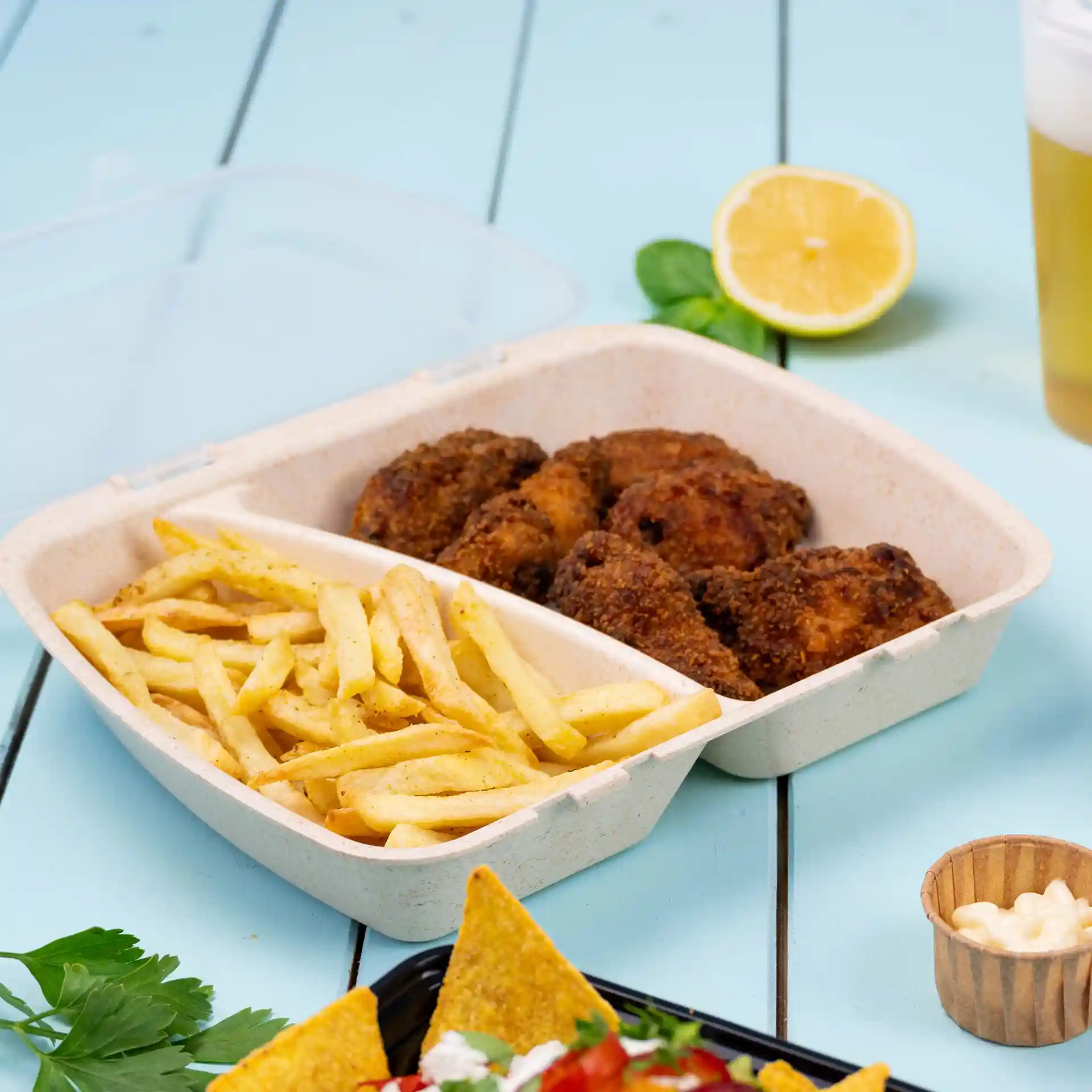 Deep reusable meal container with two compartments, containing fried chicken and French fries, on a blue surface.