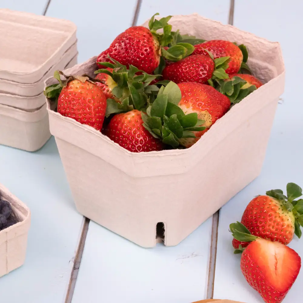 A light brown cardboard container holding fresh strawberries, with several similar containers nearby, on a blue wooden surface.