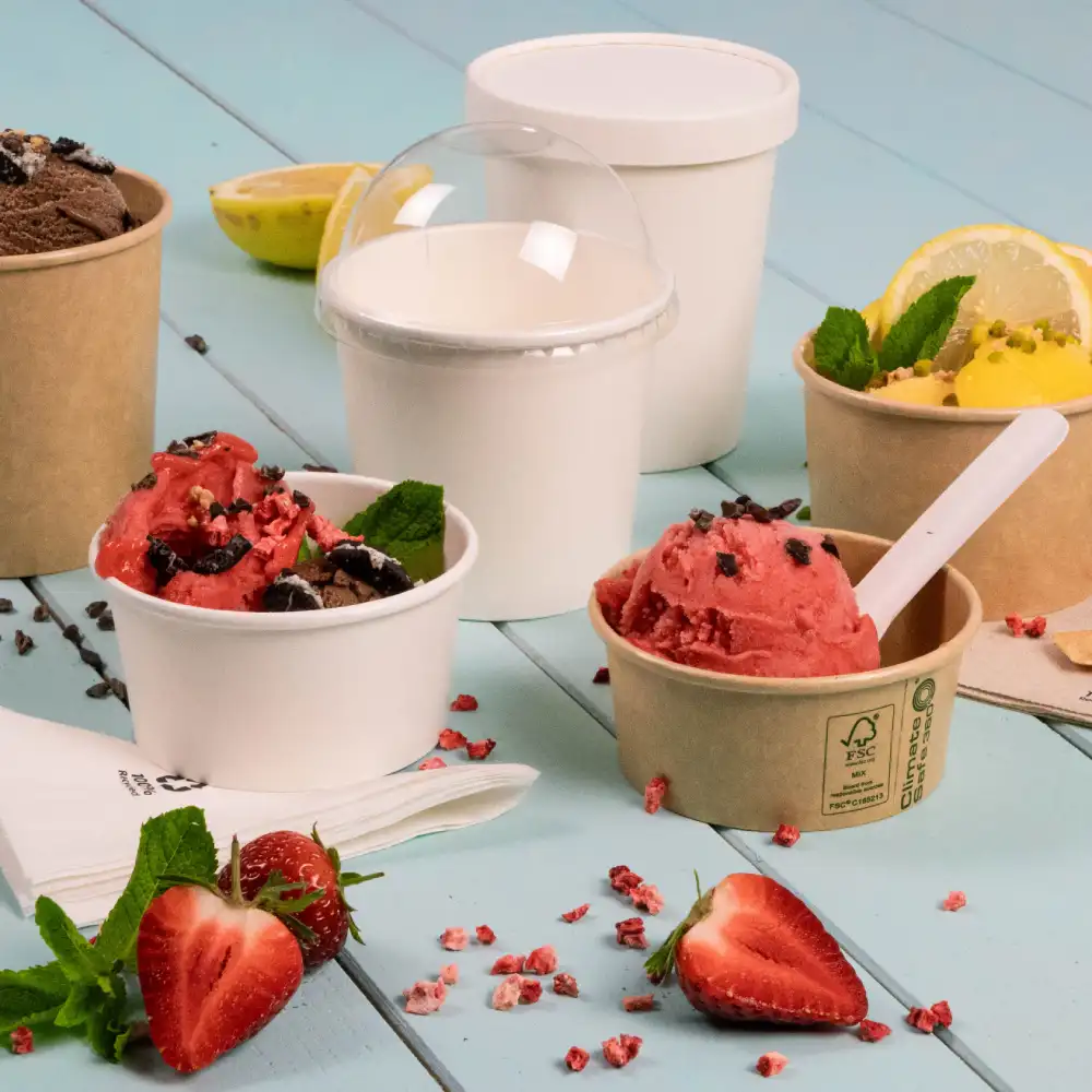 Multiple ice cream cups with flavors including chocolate and strawberry, garnished with mint leaves, on a blue wooden surface.