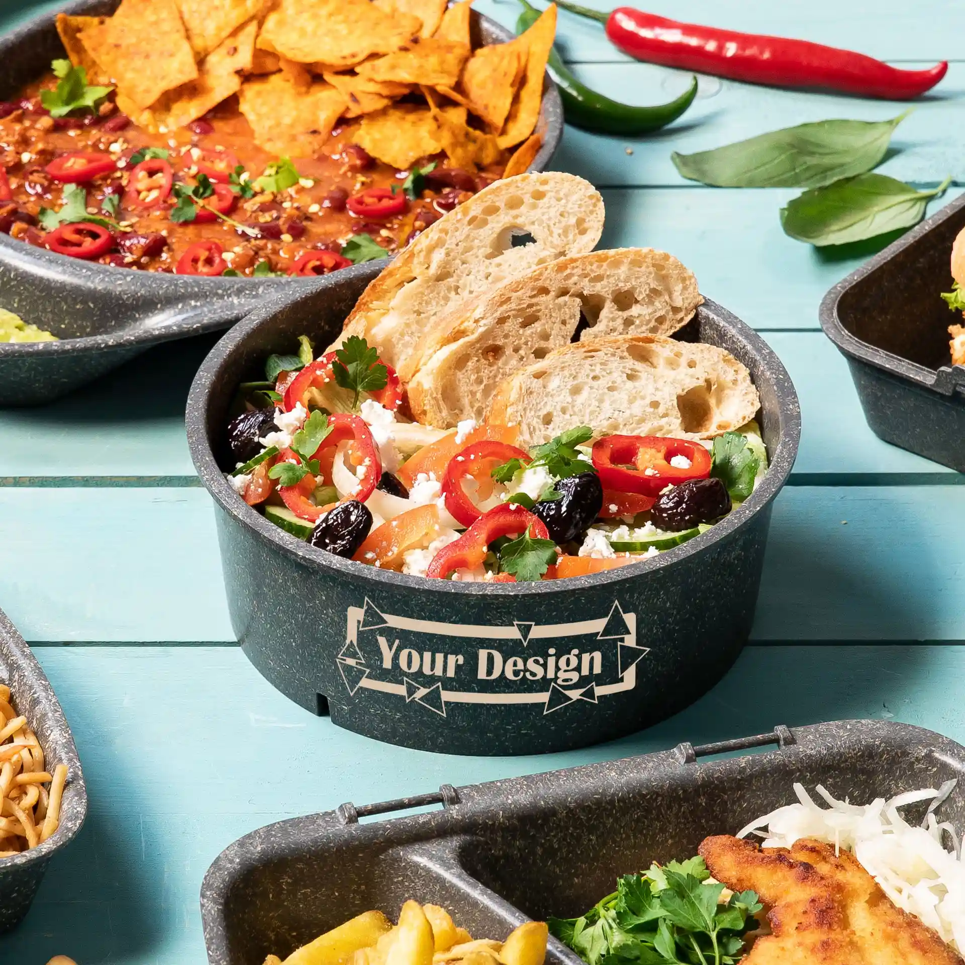 Round reusable bowl in grey with a printed design, filled with salad, bread slices, and garnished with herbs.