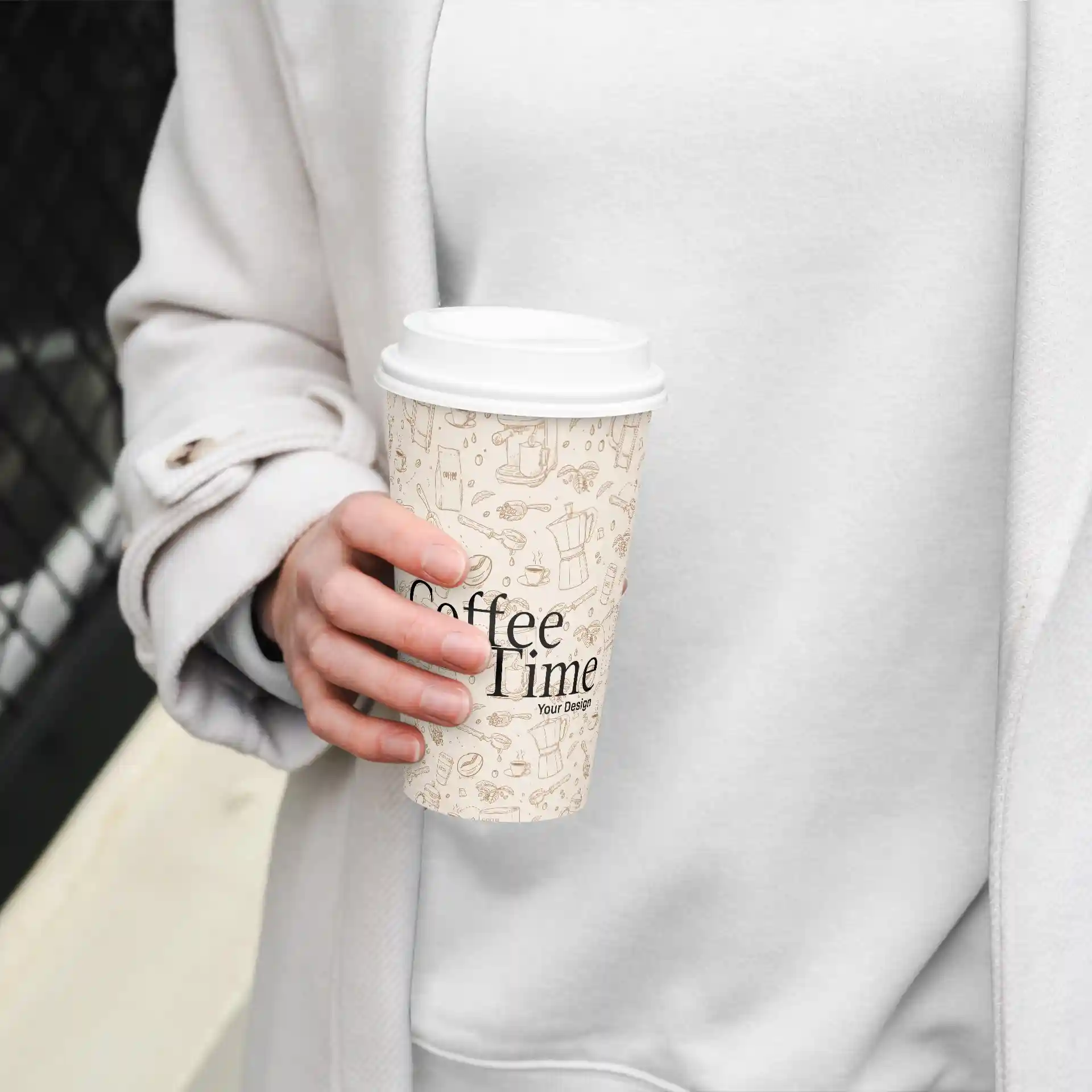 Paper cup with a white PE-coated exterior, featuring a design and held in a hand, against a light background.