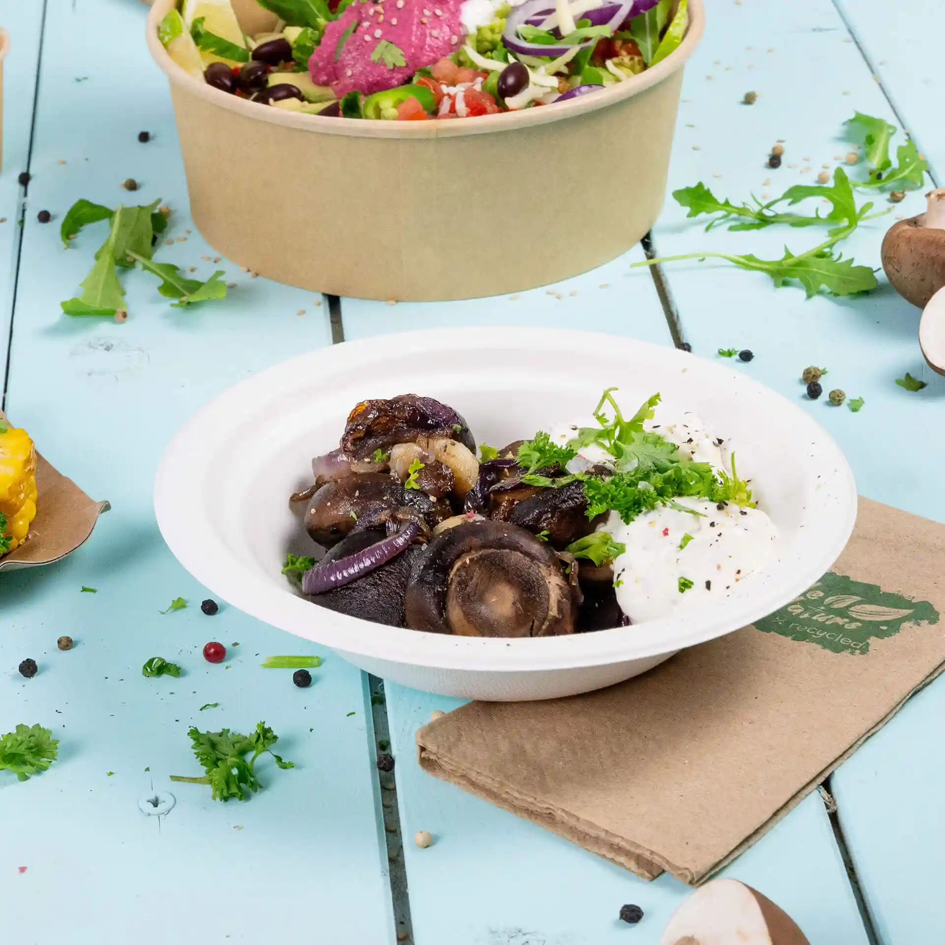 Deep round white sugarcane bowl containing cooked food, garnished with herbs, on a blue wooden surface.