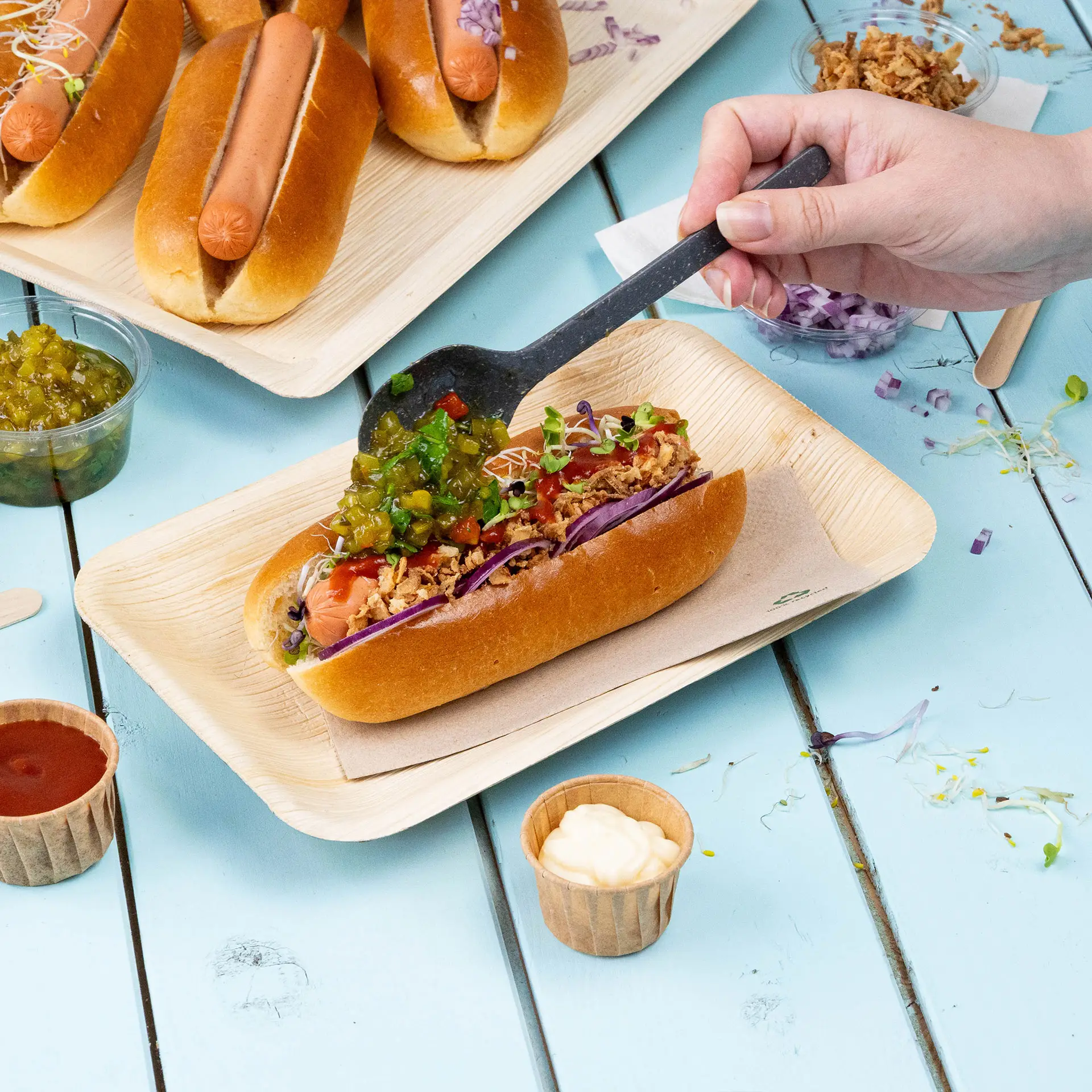 Three colorful dollops of spread on a palm leaf plate with arugula; a red radish and a silver spoon nearby, all on a turquoise wooden table.