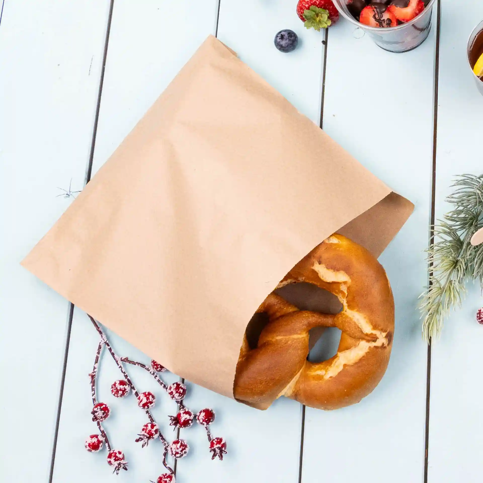 Brown kraft paper bag partially open with a pretzel visible inside, placed on a light blue wooden surface.