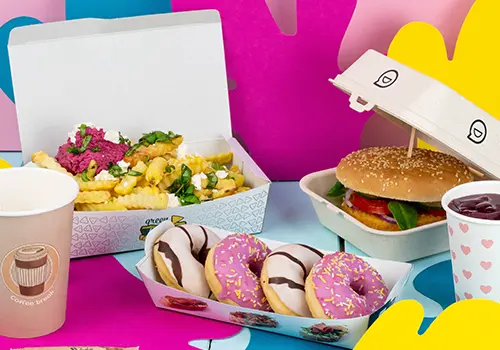 Box containing a burger with cheese, onions, lettuce, and sauces; alongside golden fries and onion rings; two small sauces included.
