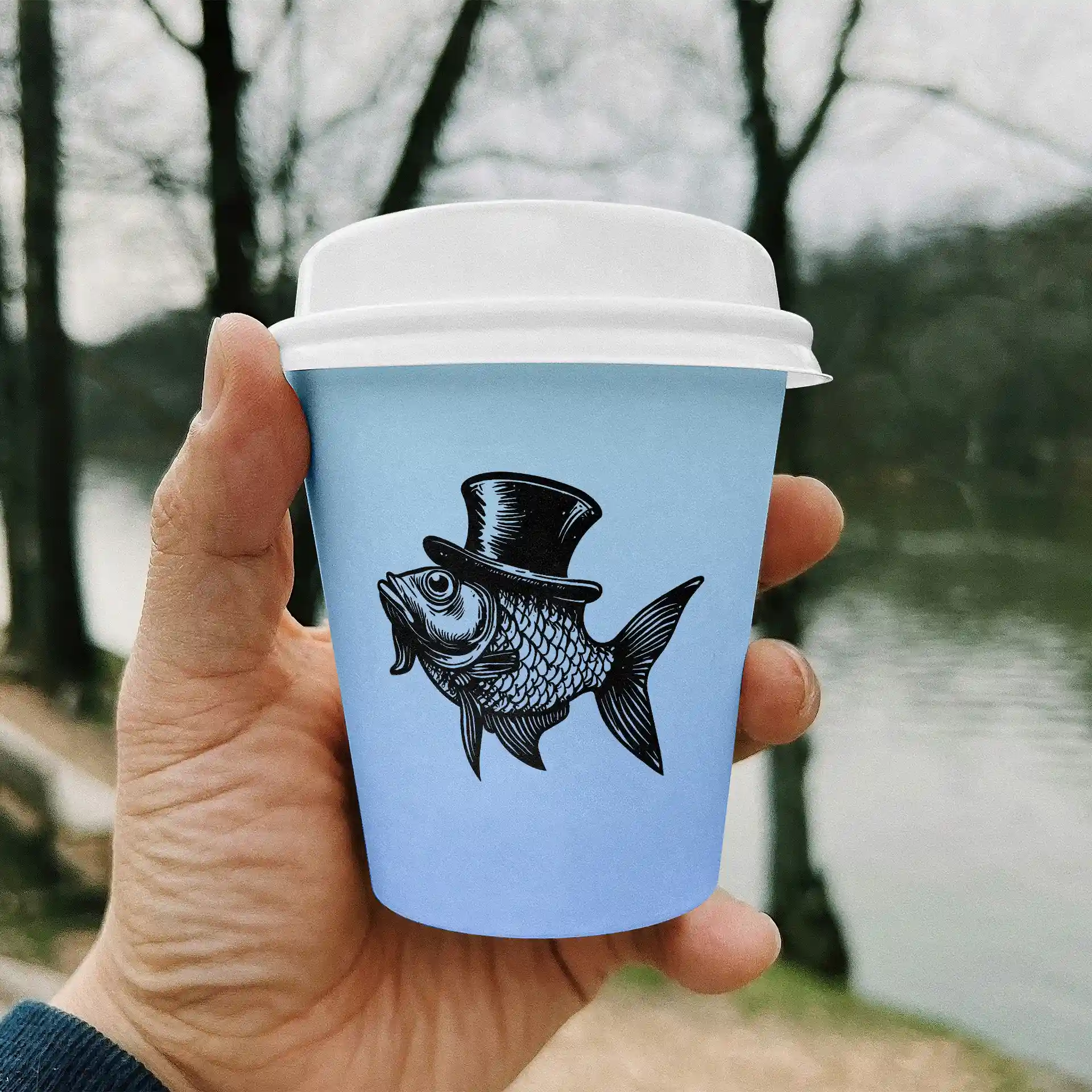 Hand holding a light blue paper cup featuring a black illustration of a fish wearing a top hat, with a blurred background.