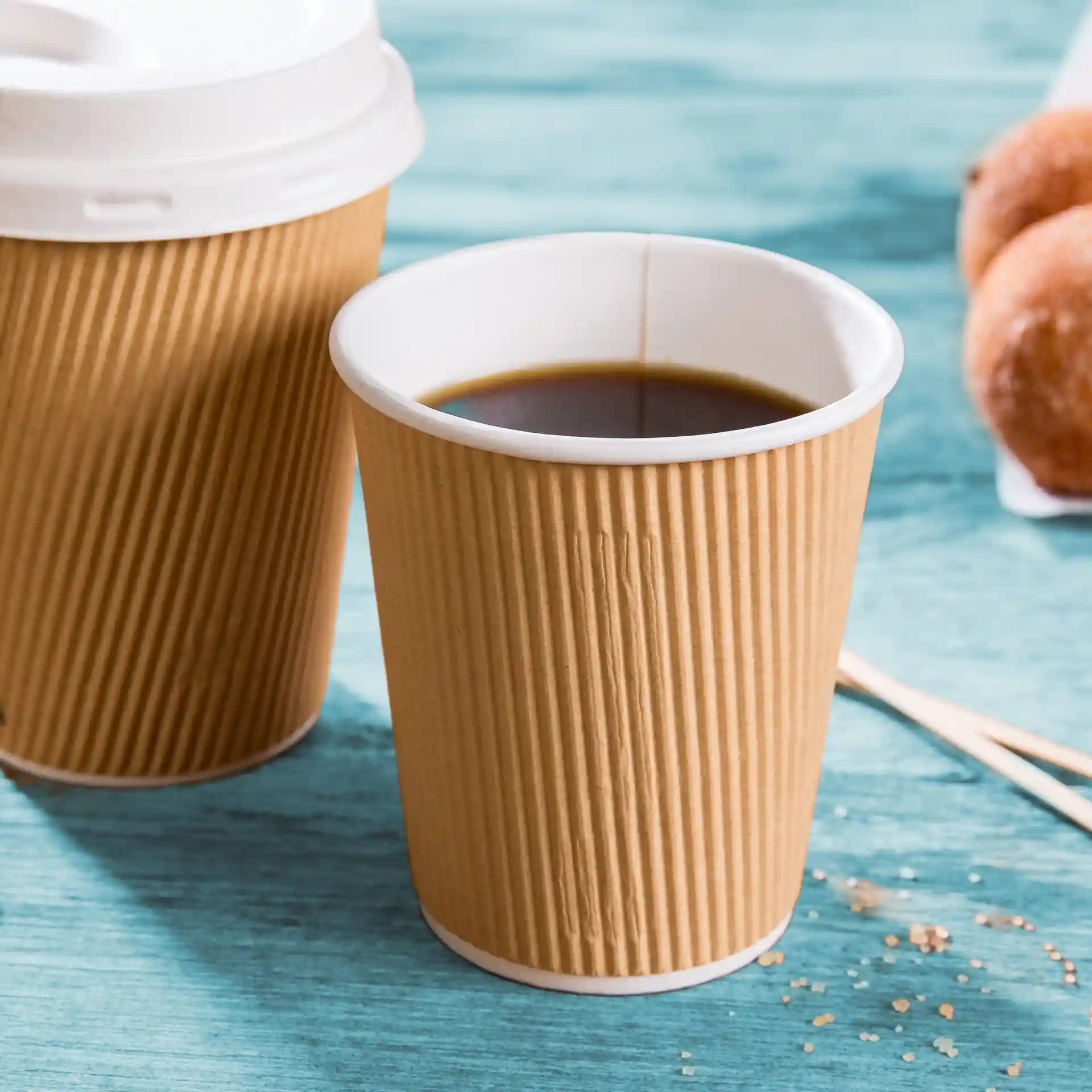 Brown ribbed coffee cup with a white interior, filled with dark liquid, on a blue surface.