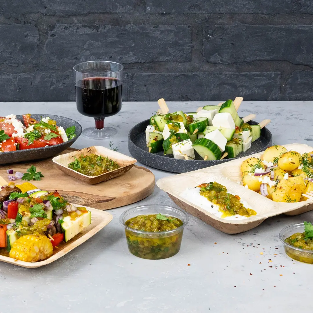 A variety of finger foods including salads, cucumber and cheese skewers, and sauces, with a glass of red wine in the background.