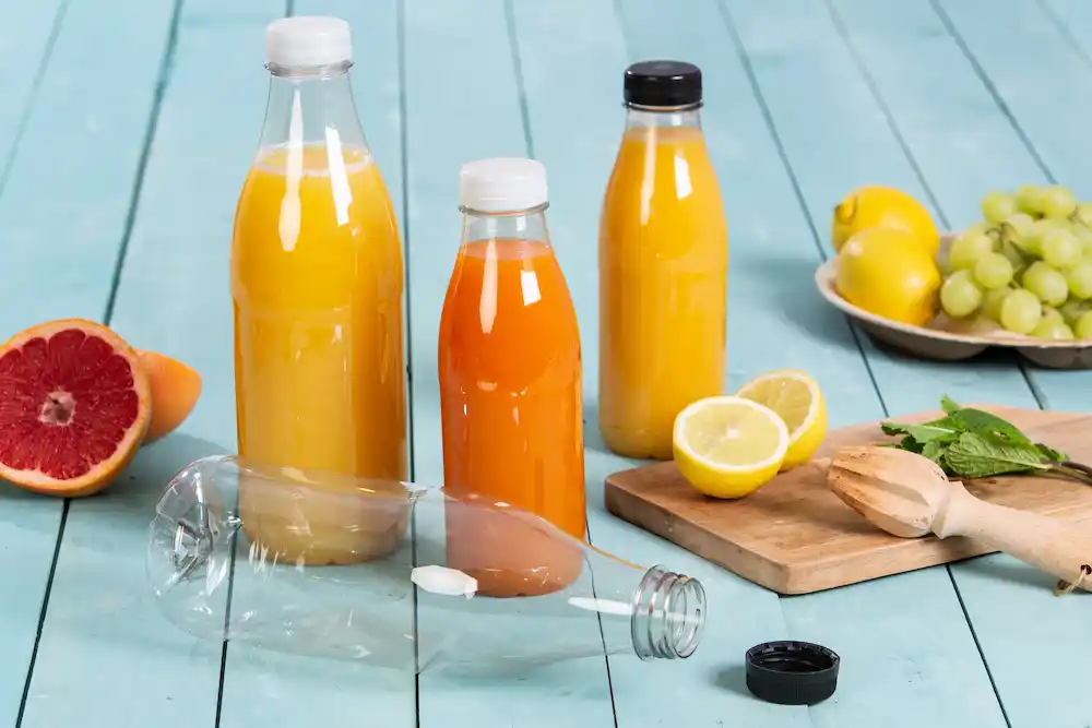 Two glass bottles filled with orange juice and yellow juice, a cut lemon, grapes, and half a grapefruit on a wooden surface.