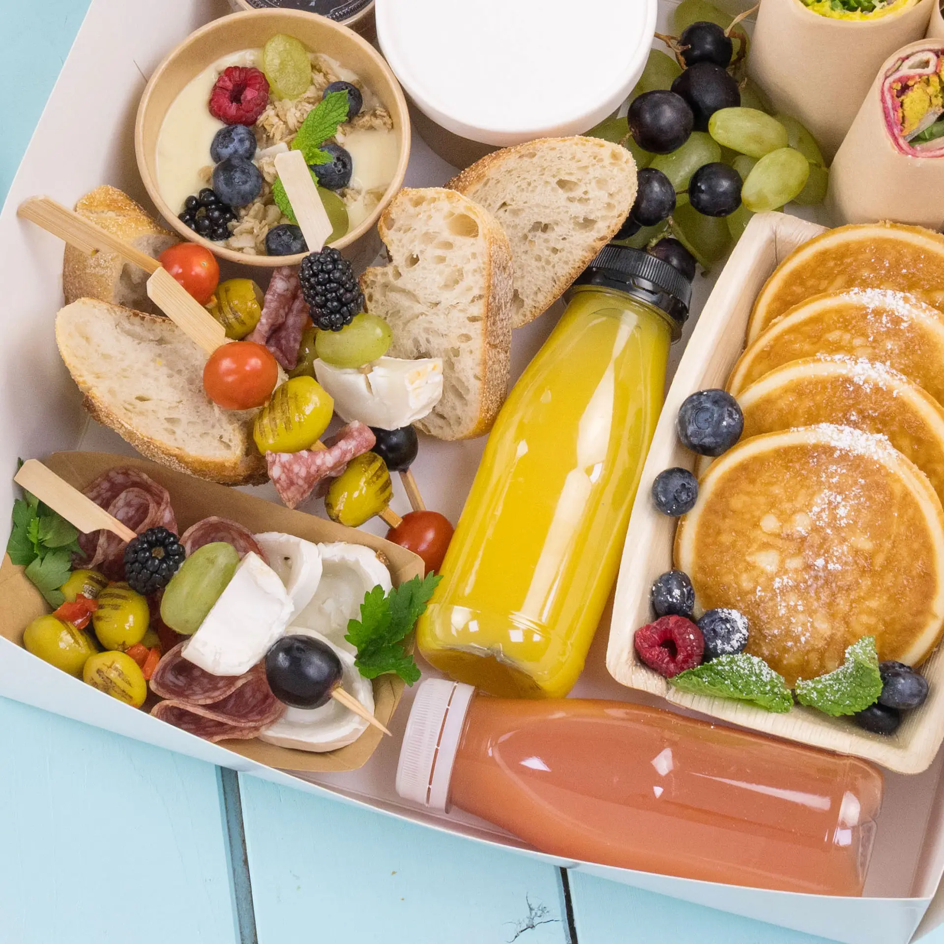 A clear bottle filled with orange beverage; accompanied by pancakes, bread, assorted fruits, and snacks in a food box.