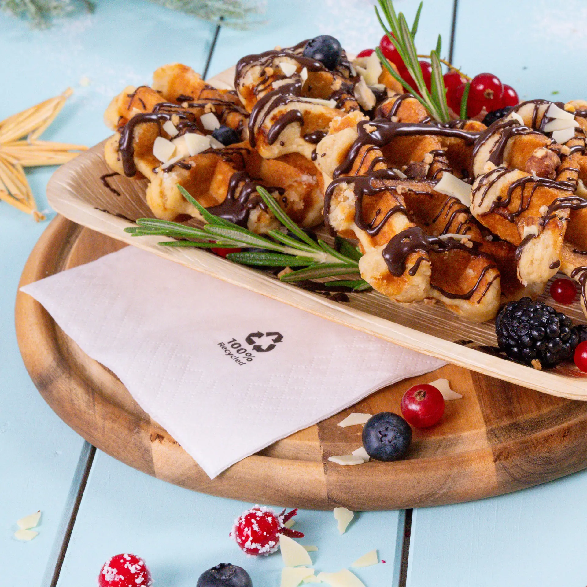 Waffles topped with chocolate drizzle and slivers of almond, served on a bamboo platter with fresh berries and a napkin.