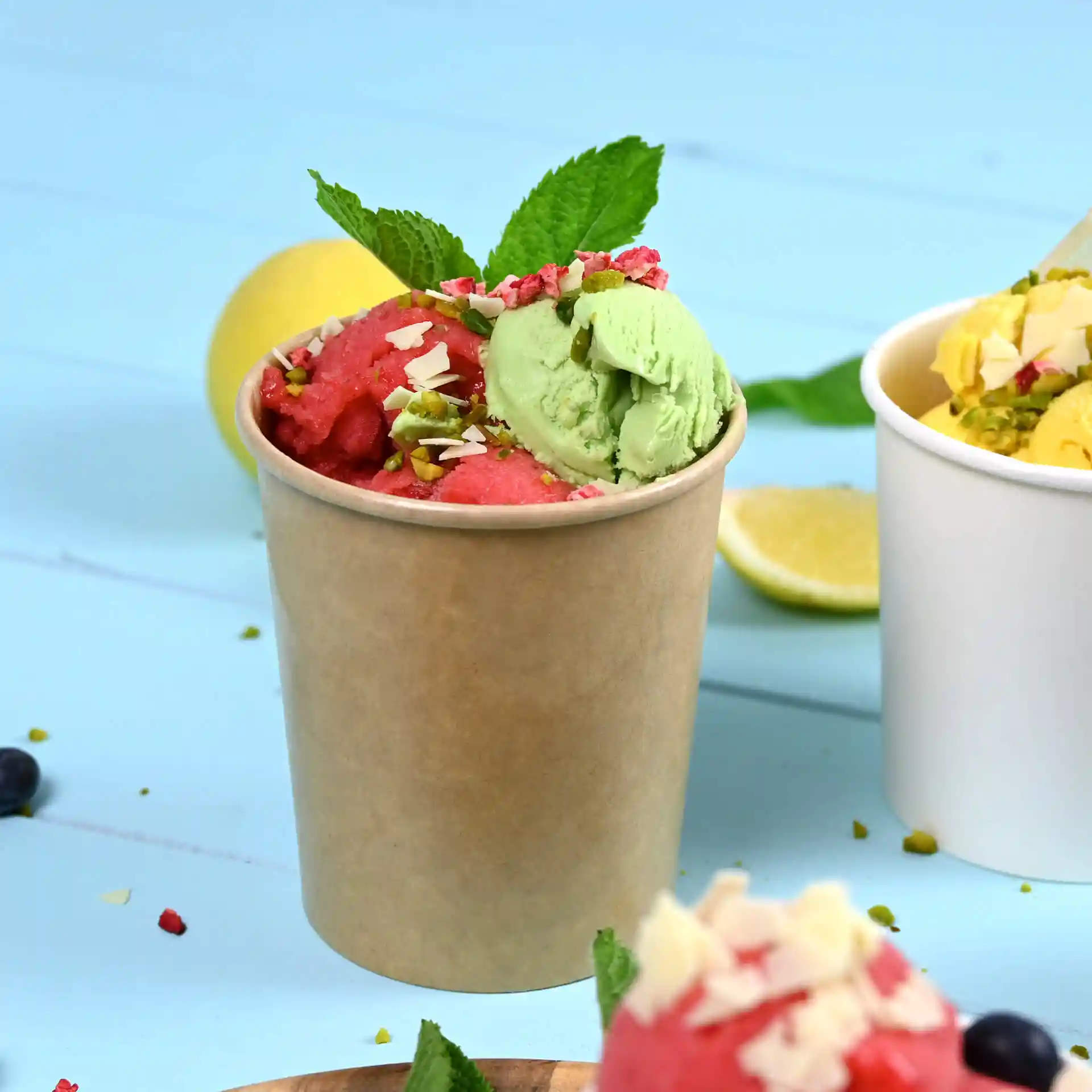 Cup filled with red and green ice cream, topped with mint leaves and nuts, on a blue background.