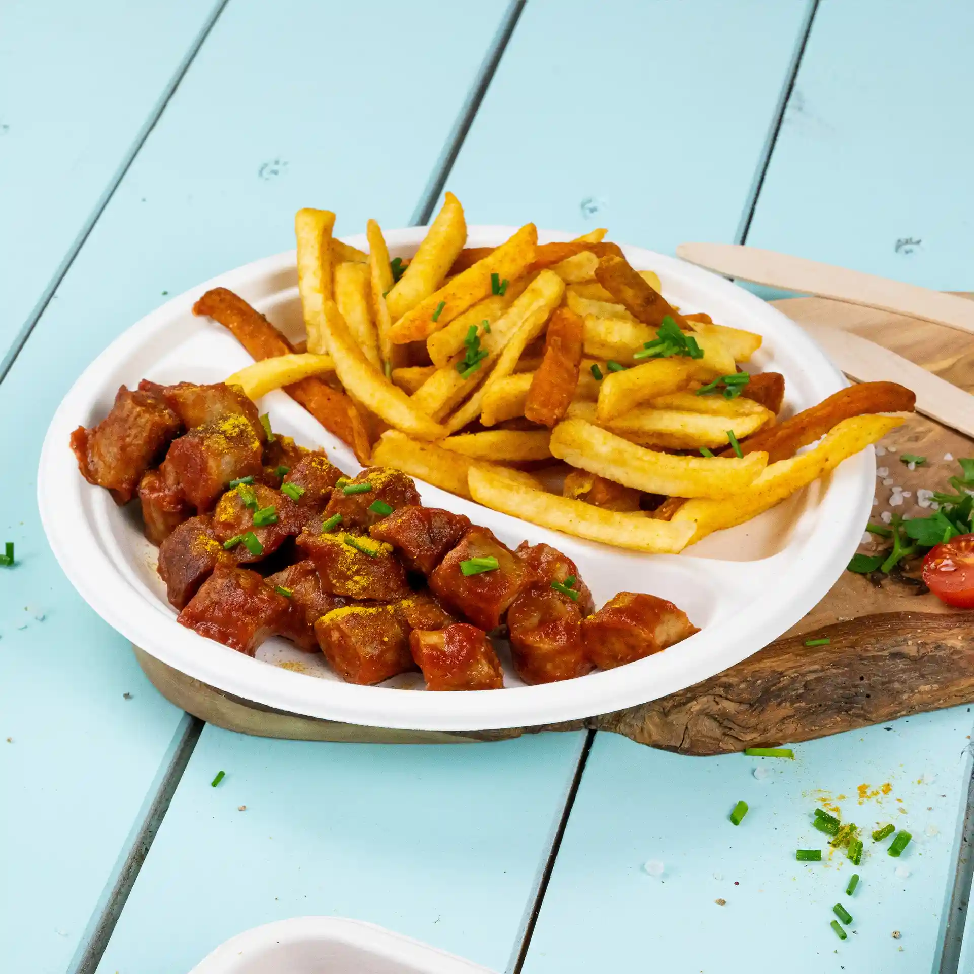 Round white sugarcane plate with two compartments, one filled with diced meat in sauce and the other with French fries.