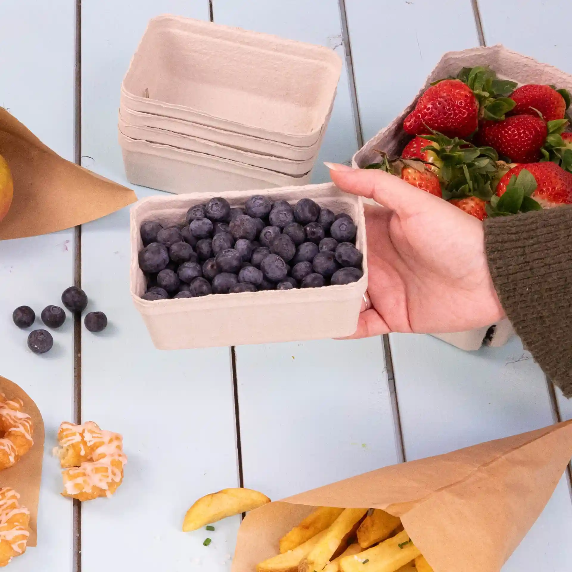 Container holding blueberries made of wood pulp, with several empty punnets stacked in the background.