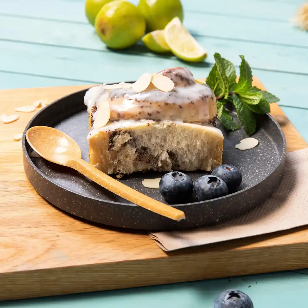 Dessert slice on a dark plate with blueberries, almond slices, a wooden spoon, and fresh mint leaves.