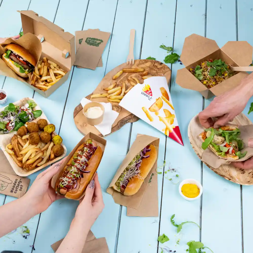 A variety of food items including hot dogs, fries, salads, and a dipping sauce on a blue wooden table.