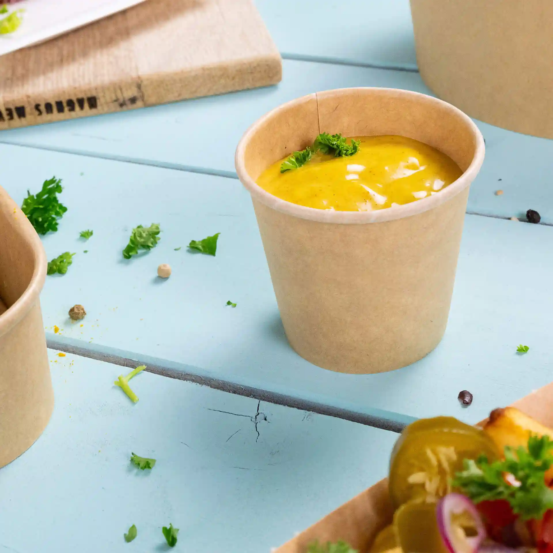 Brown paper portion cup with eco-friendly coating, filled with sauce and topped with a small piece of parsley.