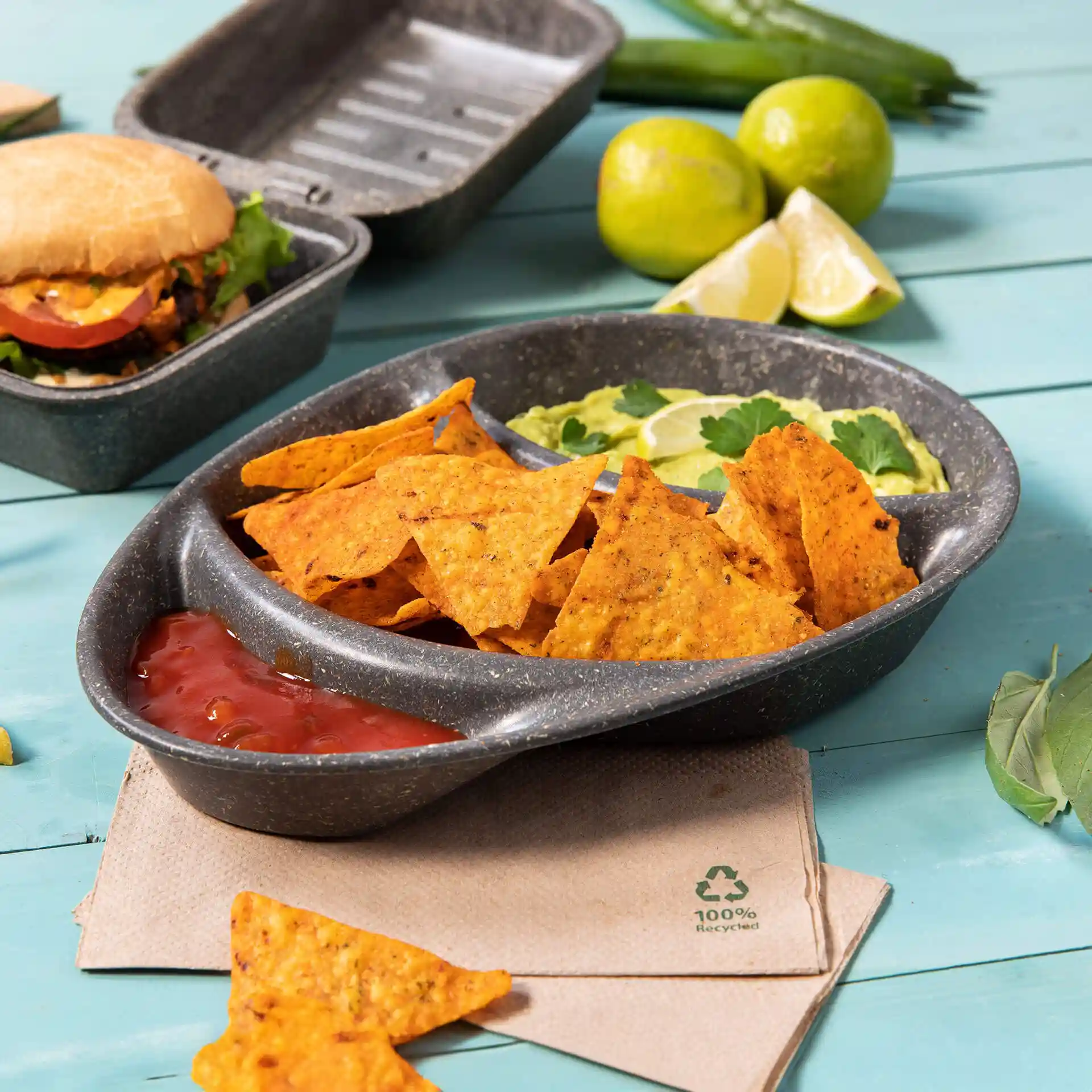Reusable divided plate with three compartments, filled with nachos, salsa, and guacamole, on a blue surface.