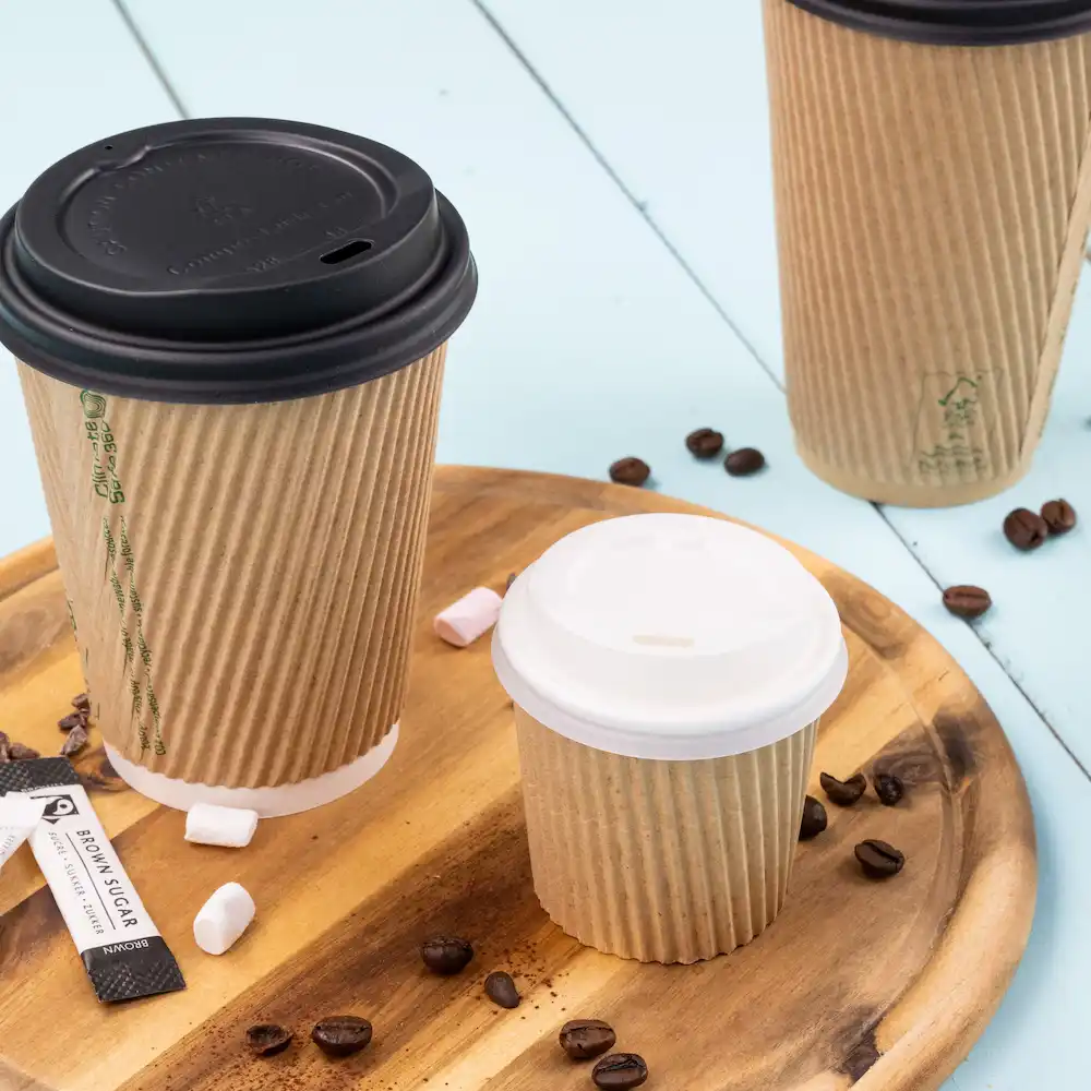 Three paper coffee cups of varying sizes with lids, placed on a wooden tray with coffee beans and sugar packets.