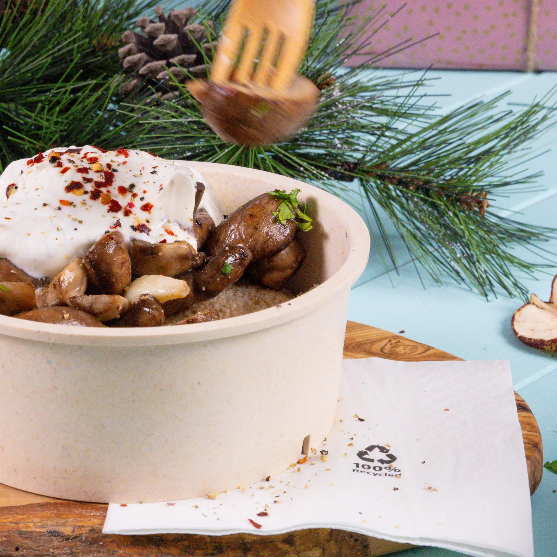 Freshly prepared dish in a brown cardboard bowl topped with yogurt, herbs, and spices; accompanied by a white recycled cocktail napkin.