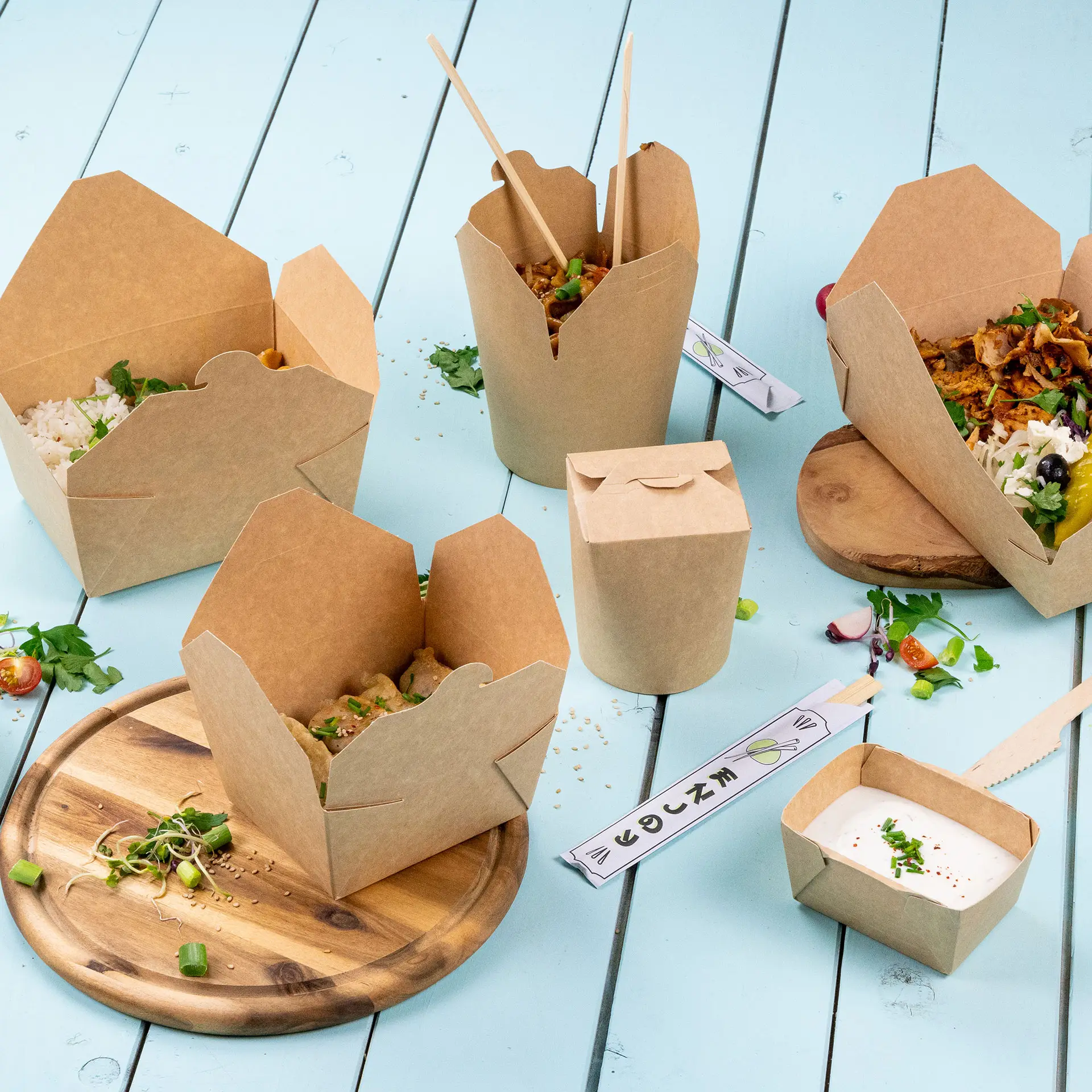 Takeaway boxes in various styles on a blue surface; includes cardboard containers with food, chopsticks, and a small sauce cup.