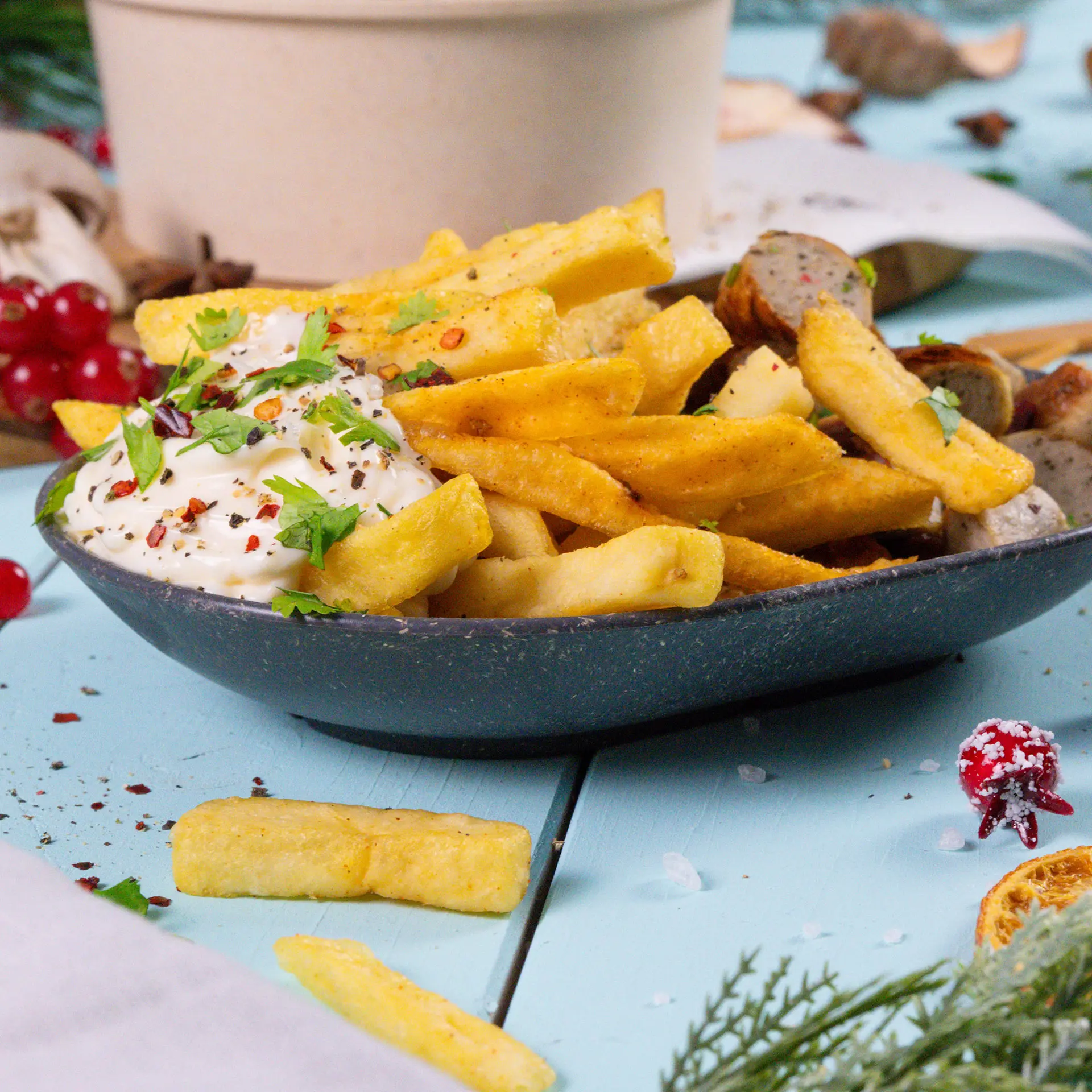 One oval reusable snack bowl filled with French fries topped with red chilies and cilantro; nearby are green and red peppers, fork, and snacks.