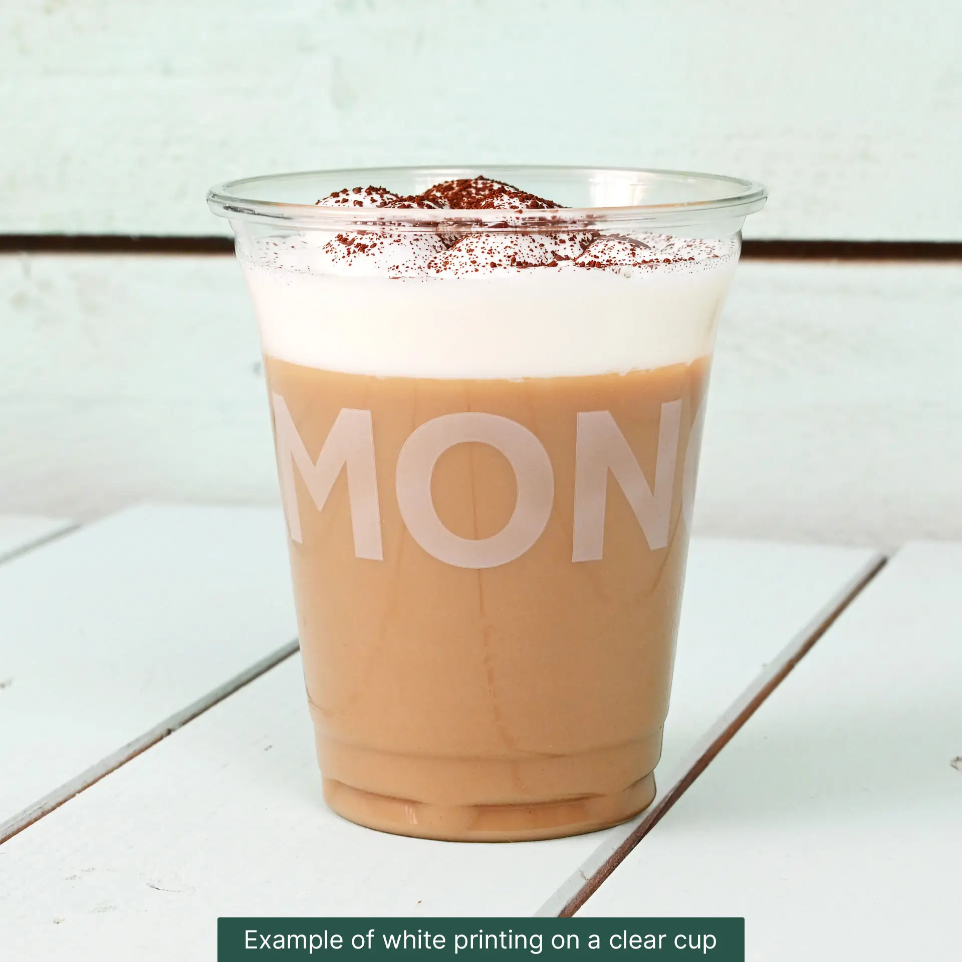 Clear 10 oz PLA cup filled with iced coffee, topped with whipped cream and cocoa powder, set against a light background.