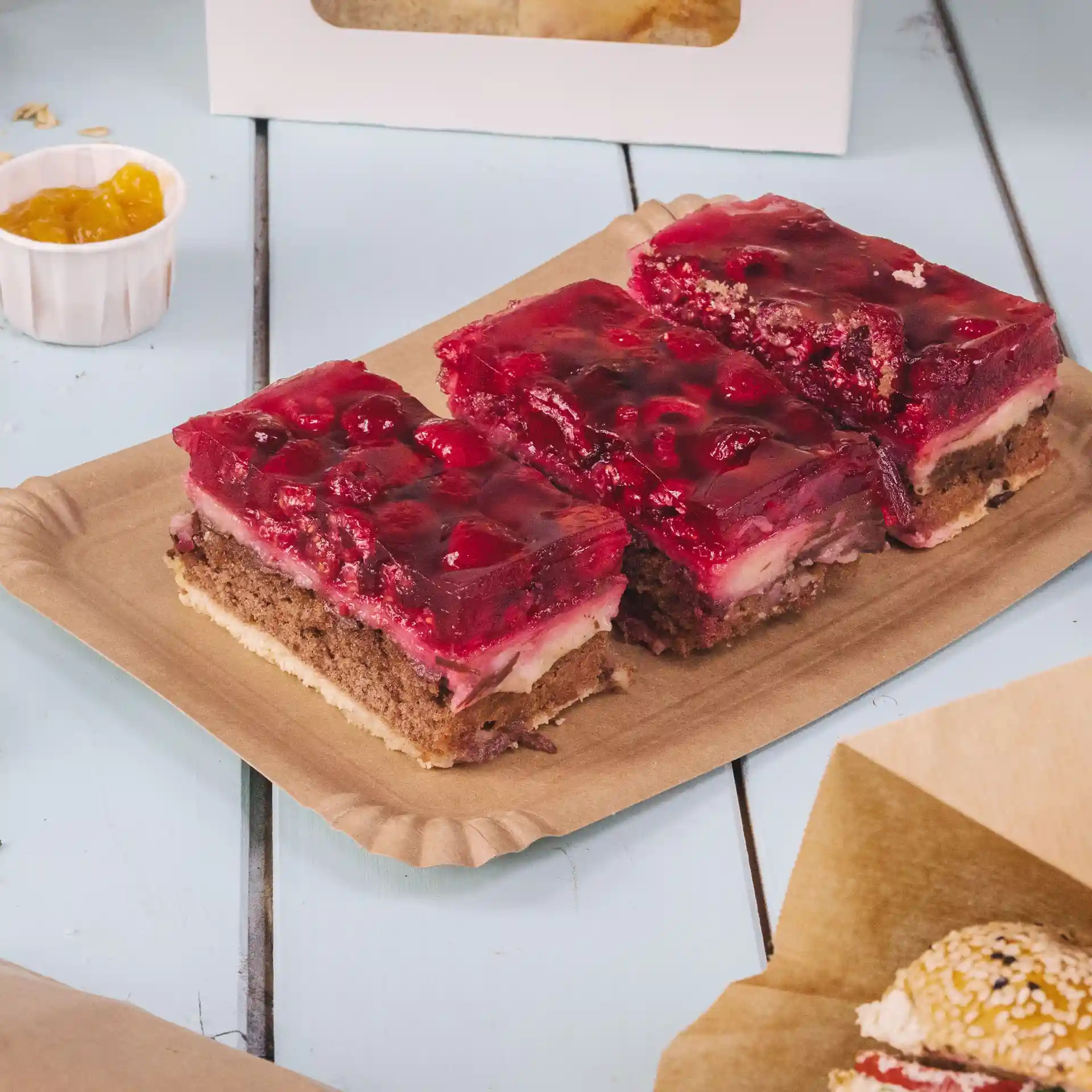 Rectangular brown cardboard plate with several layers of cake topped with red jelly and fruit pieces.