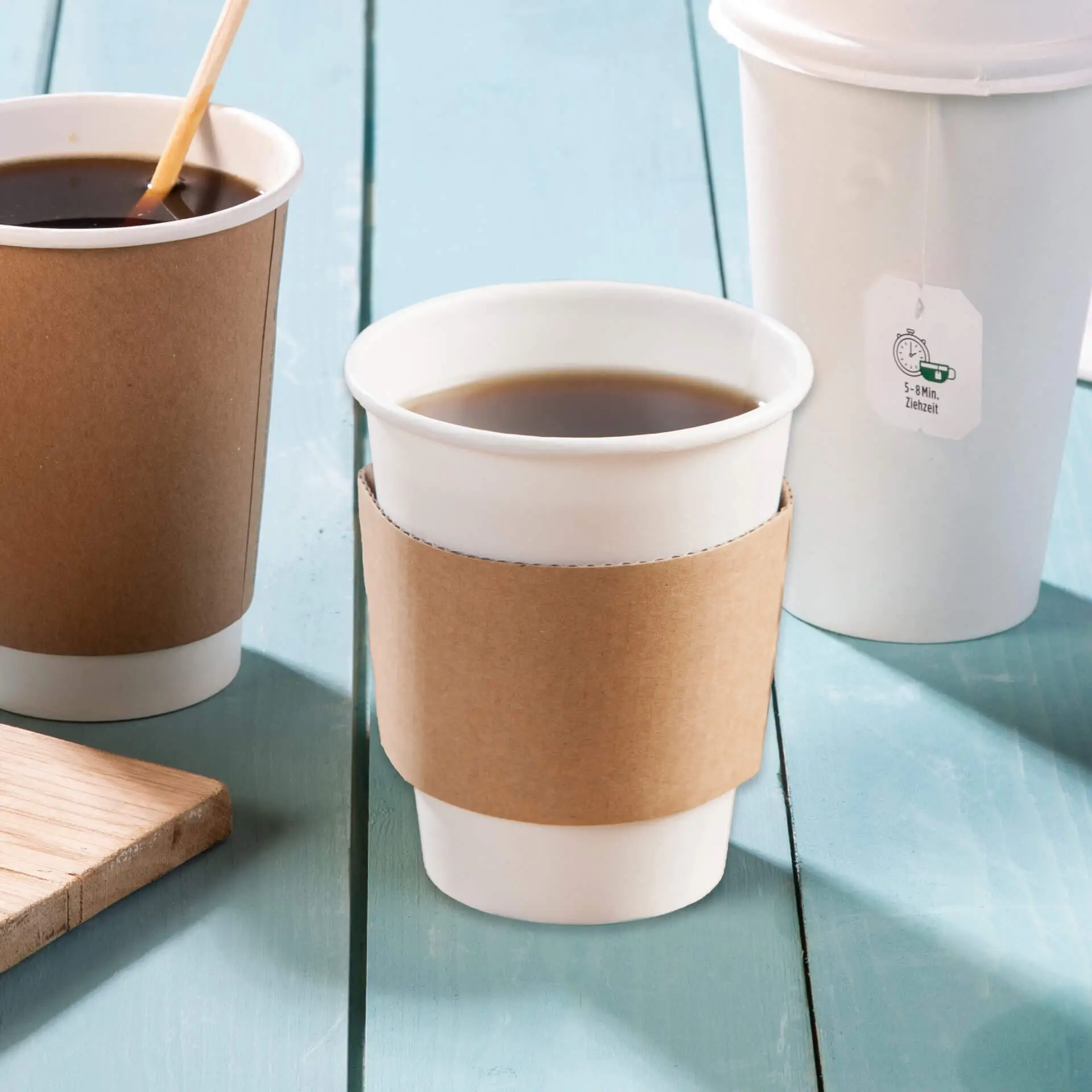 Brown cardboard cup sleeve on a white paper coffee cup, surrounded by similar cups on a blue wooden surface.