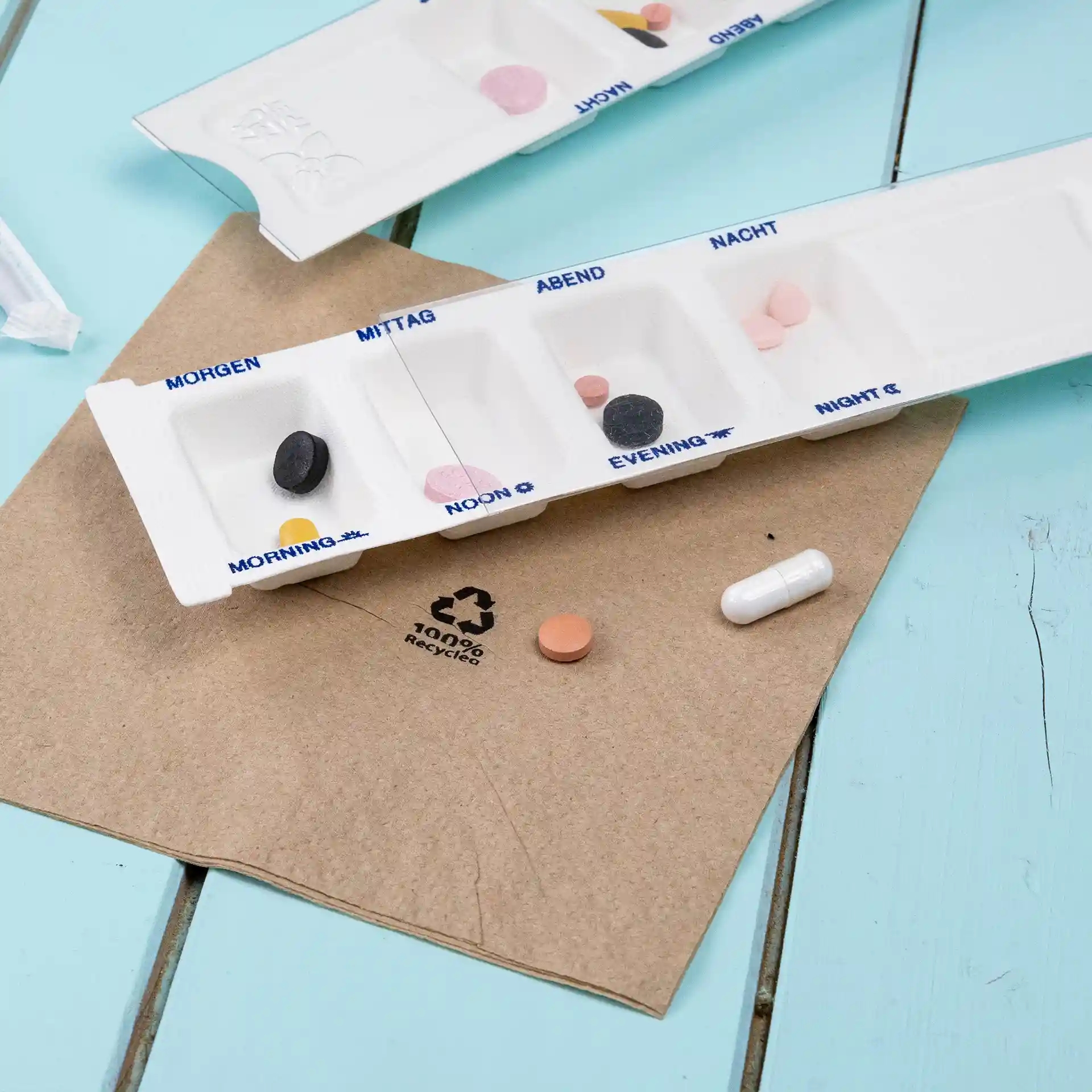Medication dispenser with four chambers, white, on a brown surface with various colored pills nearby.