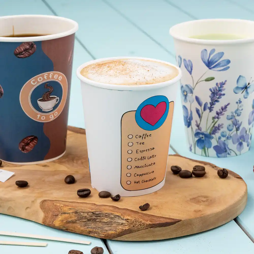Three paper cups filled with beverages, including a coffee cup with a checkbox list for drink options, on a wooden surface.