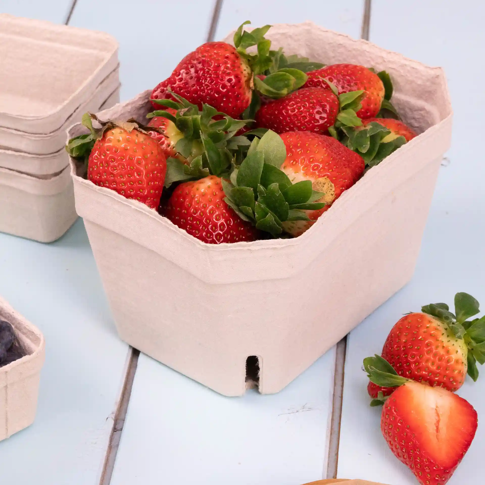 Container made of wood pulp holding several strawberries, with additional empty containers in the background.