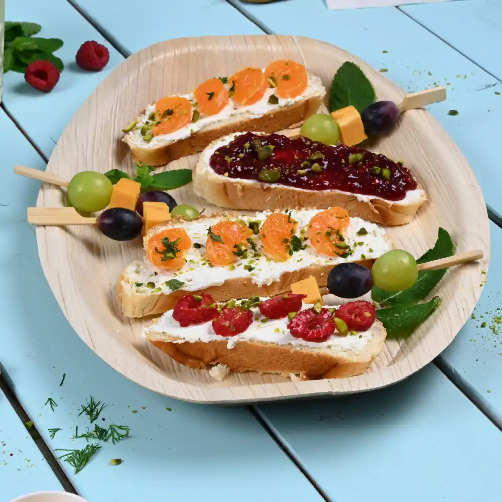 Four slices of bread topped with various spreads and garnishes on a wooden platter, featuring fruits and herbs.