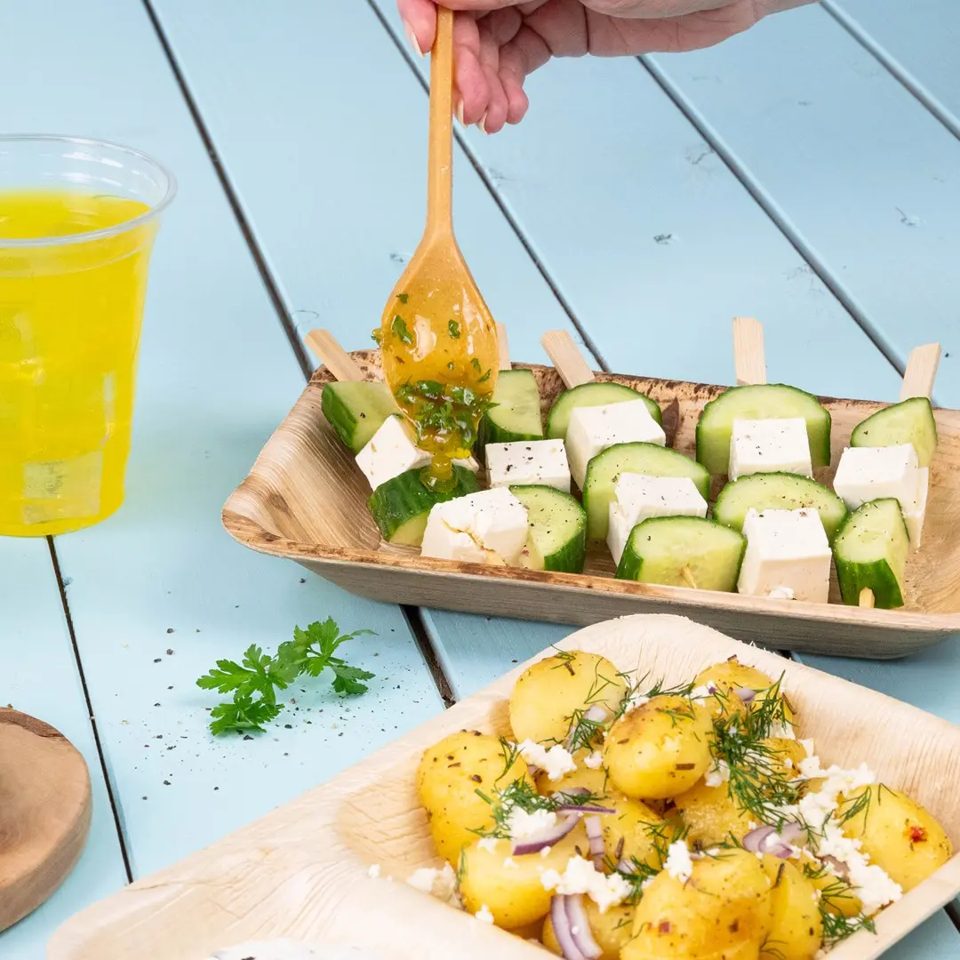 Wooden skewers with cucumber and cheese cubes, served with a side of seasoned potatoes and a drink.