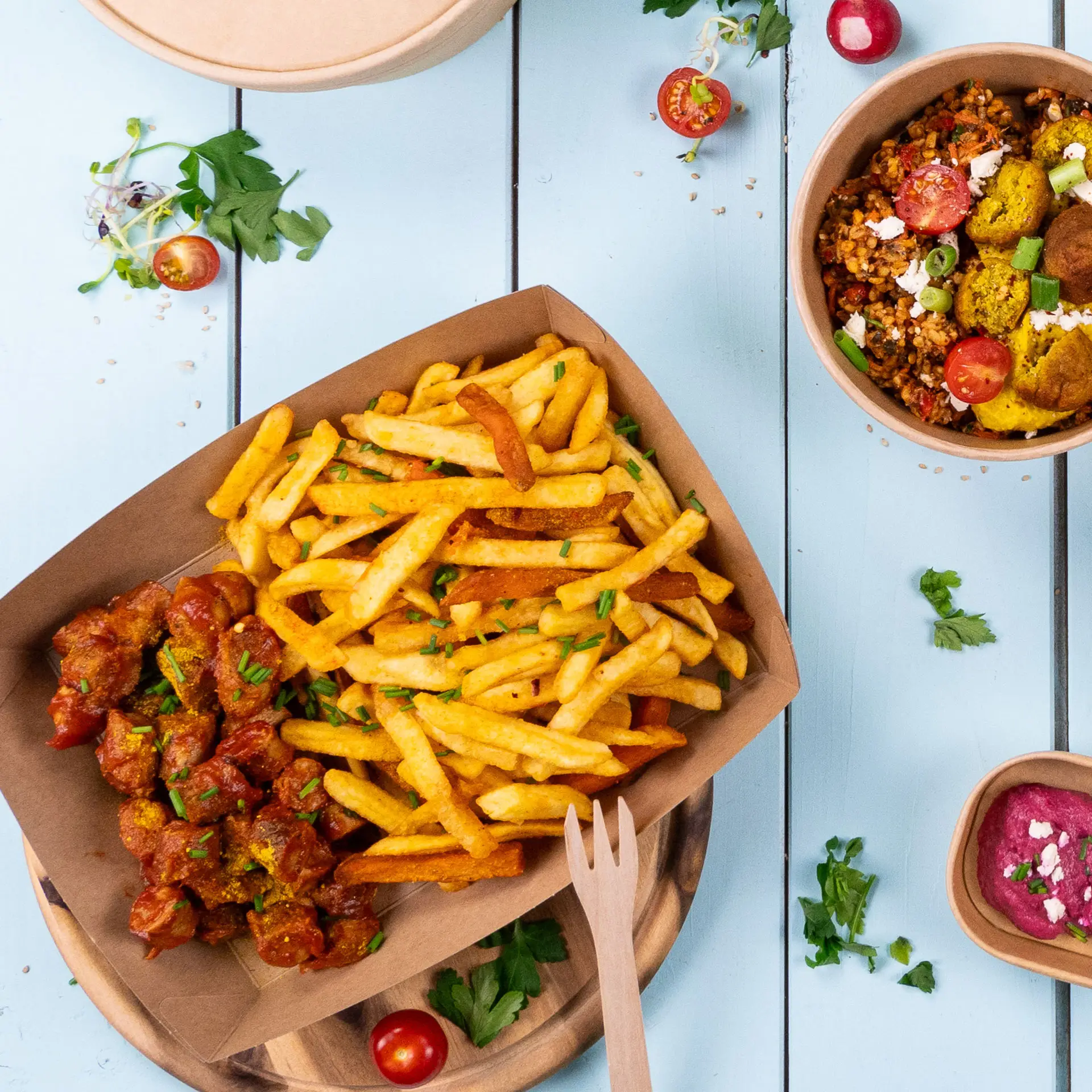 Cardboard tray filled with golden fries and spicy meatballs, garnished with herbs, on a blue wooden surface.