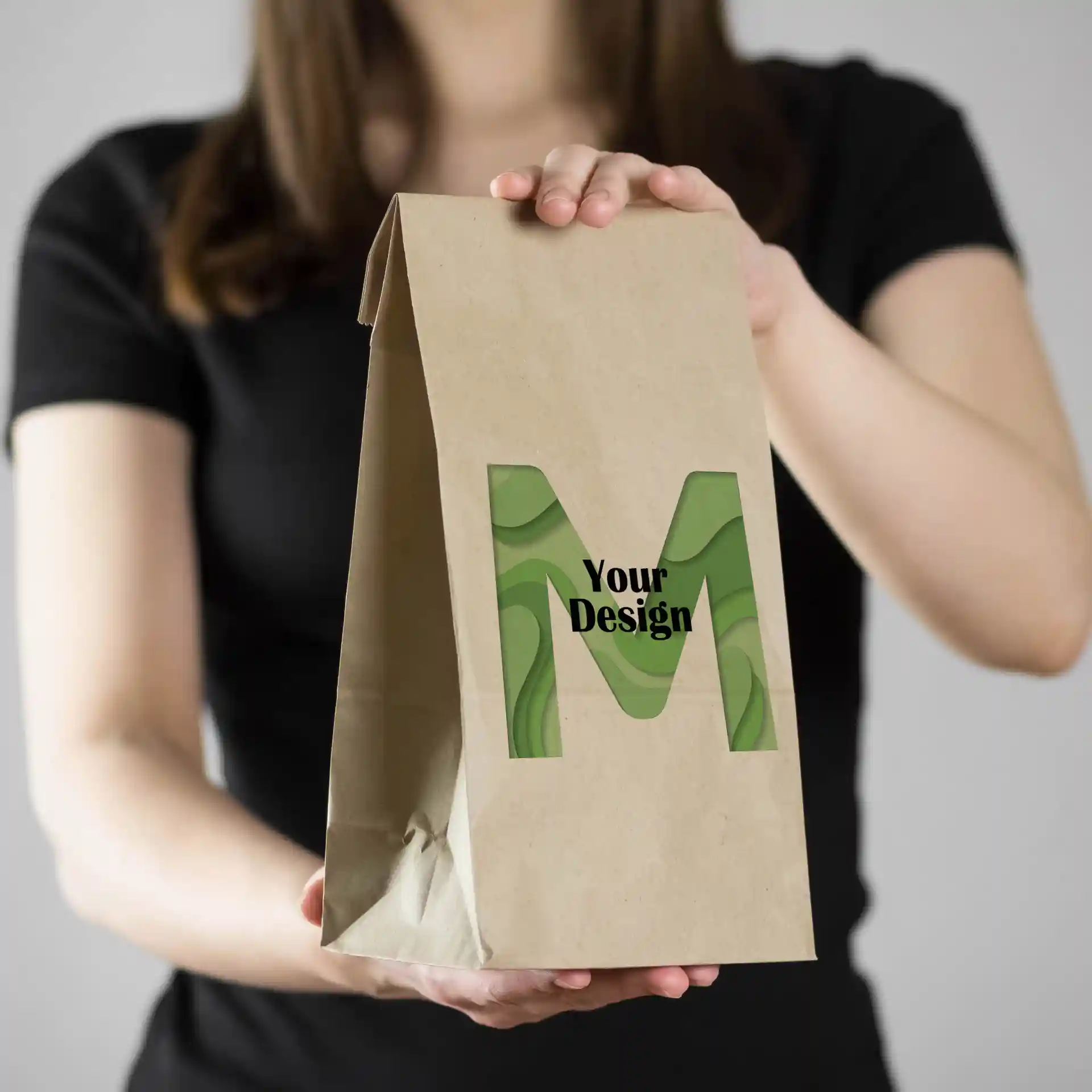 Brown printed paper bag featuring a green "M" design, held by a person in a black shirt.
