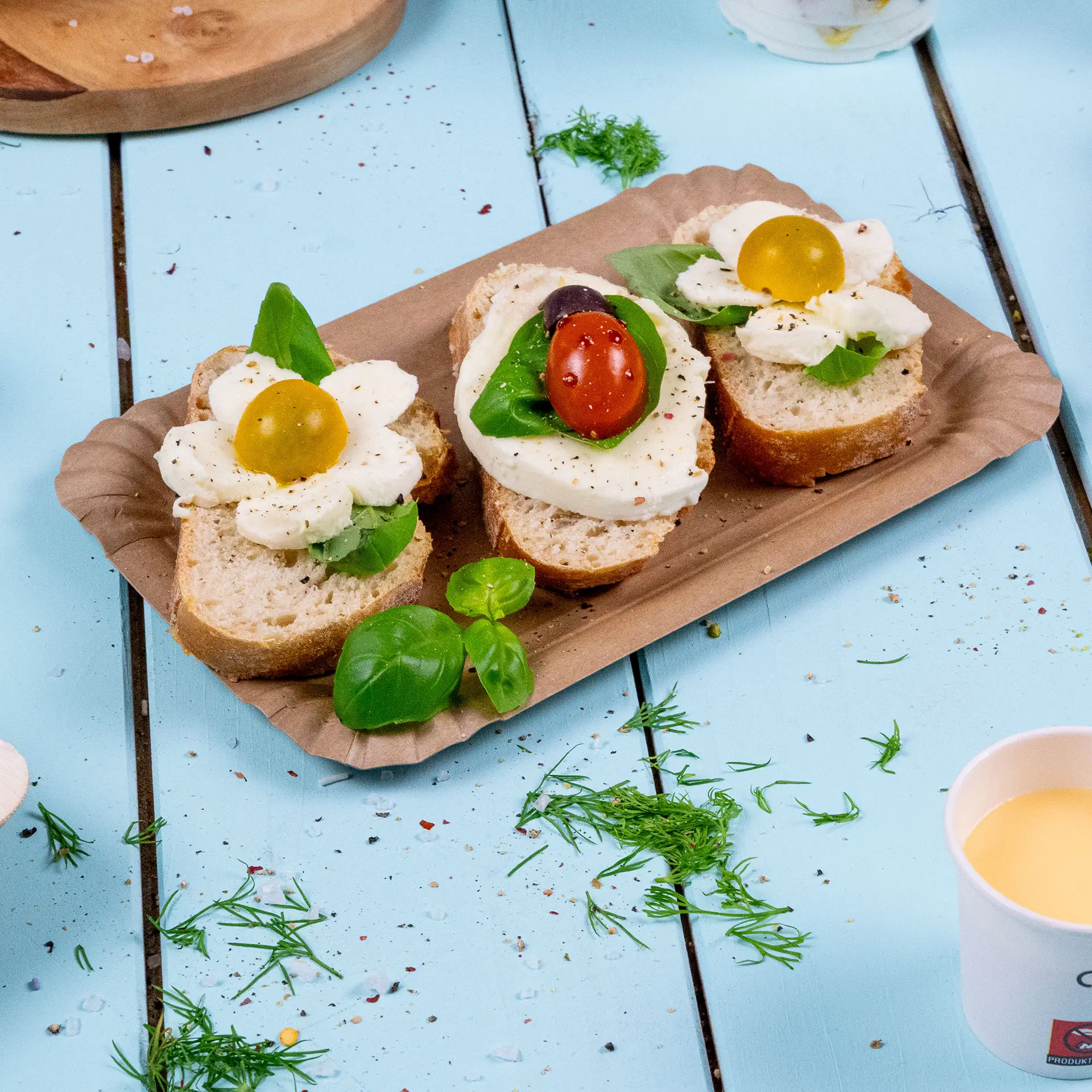 A rectangular brown cardboard plate holds two open-faced sandwiches topped with mozzarella, basil, and cherry tomatoes.