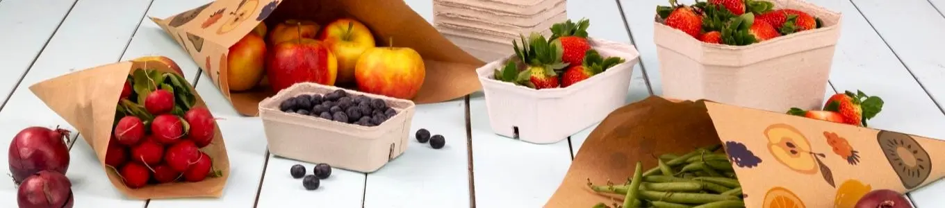 Assorted fruits and vegetables in paper cones and containers on a light wooden surface.