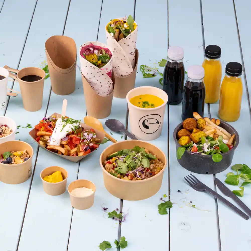 Assorted food items in eco-friendly packaging, including wraps, salads, soups, and beverages on a blue wooden surface.