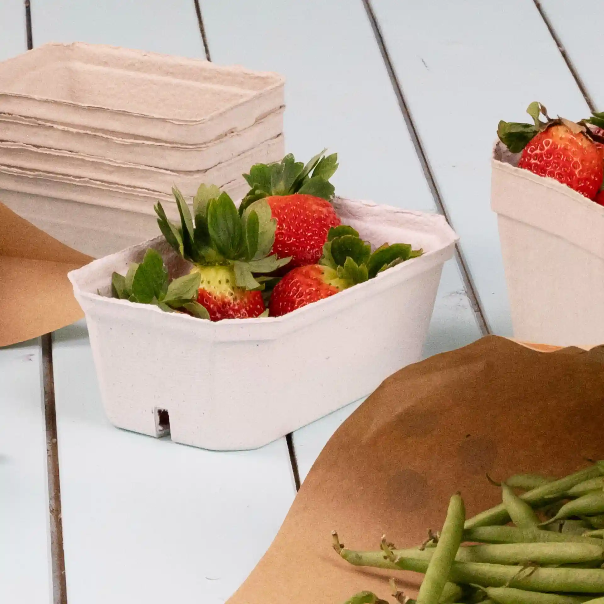 Container holding strawberries, made of white wood pulp, with additional empty containers in the background.
