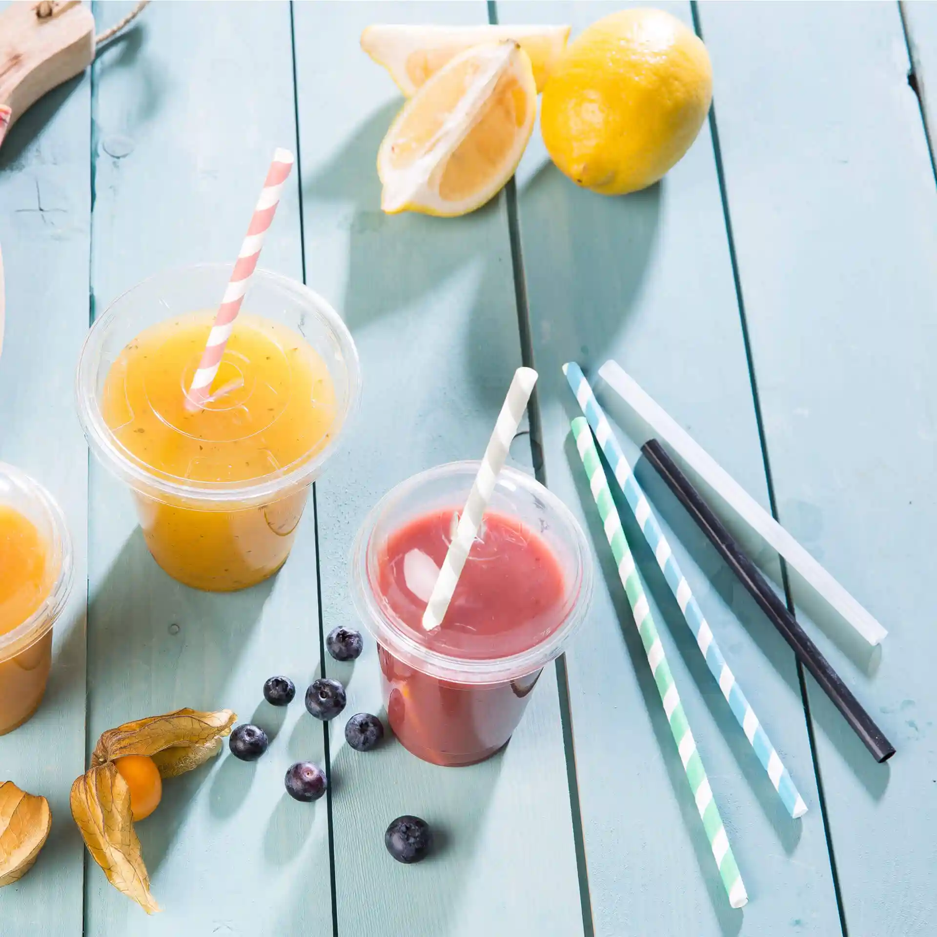 Image of two clear cups with drinks, one orange and one red, with paper straws, and several pastel striped straws on a blue wooden surface.