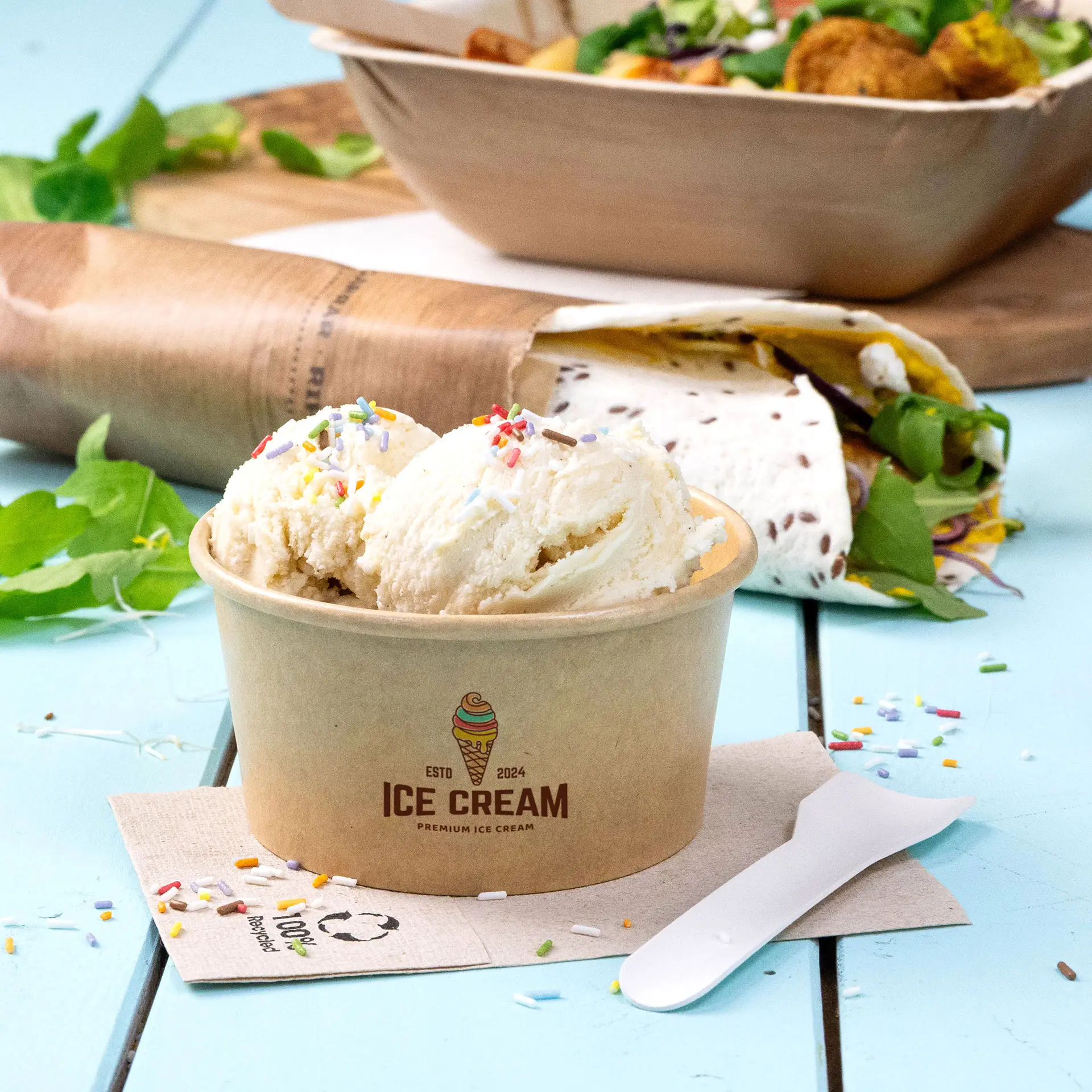 Custom printed brown ice cream cup with two scoops of ice cream and colorful sprinkles, with a spoon and background items.